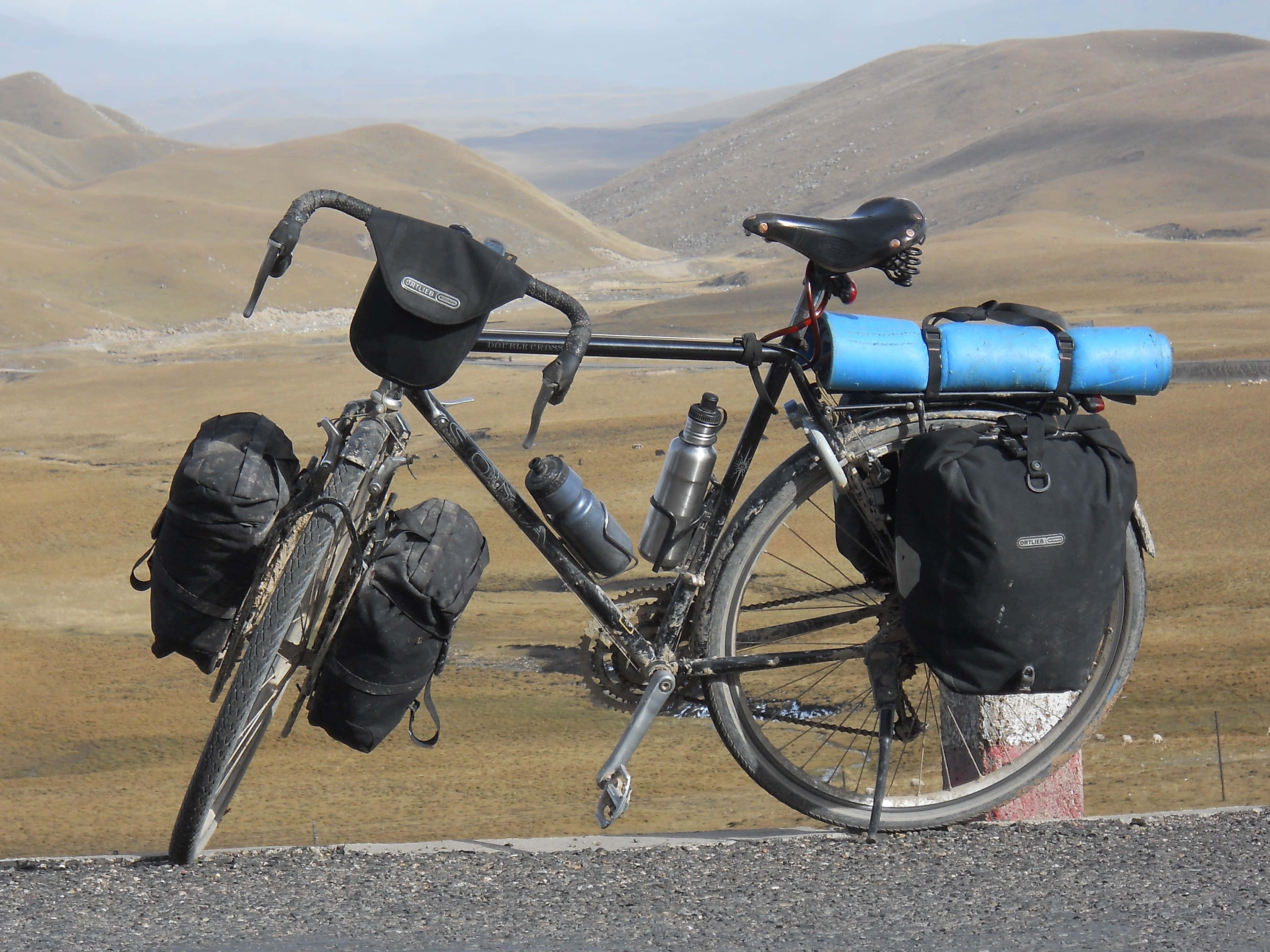 Bicycle 桌布 壁紙 — 一輛裝載著裝備的堅固旅行單車在路邊休息，背景是朦朧天空下起伏的金色山丘。