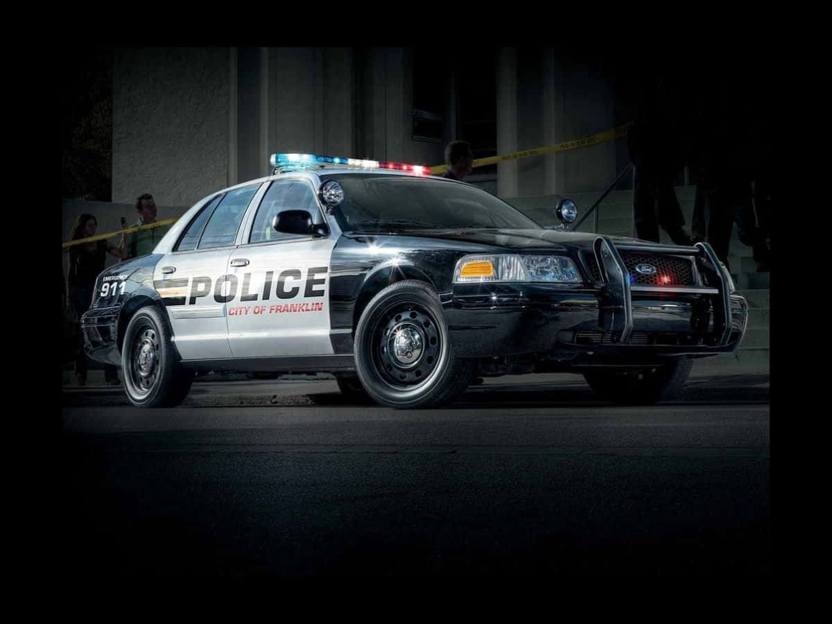 Ford Crown Victoria 桌布 壁紙 — 一輛警車在夜間閃著燈停在犯罪現場膠帶附近，背景有警員。