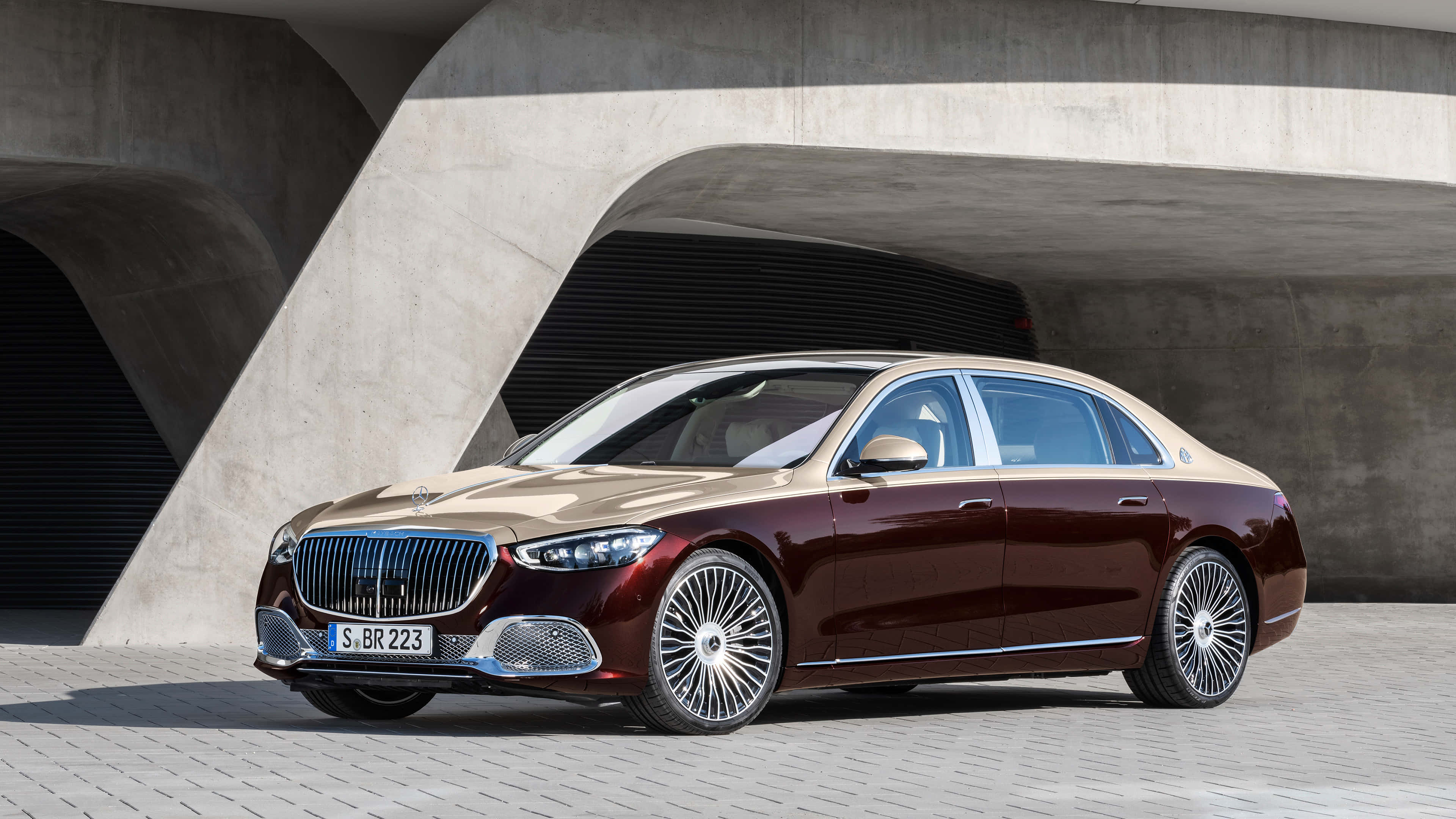 4K Mercedes 桌布 壁紙 — 一輛豪華的梅賽德斯-邁巴赫S級轎車，酒紅色和香檳色，停放在現代混凝土拱門下。