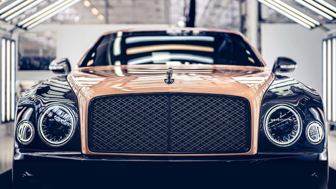 Bentley Mulsanne 桌布 壁紙 — 一輛豪華的玫瑰金賓利Bentayga在明亮的車間燈光下閃閃發光，展示其標誌性格柵和圓形頭燈。