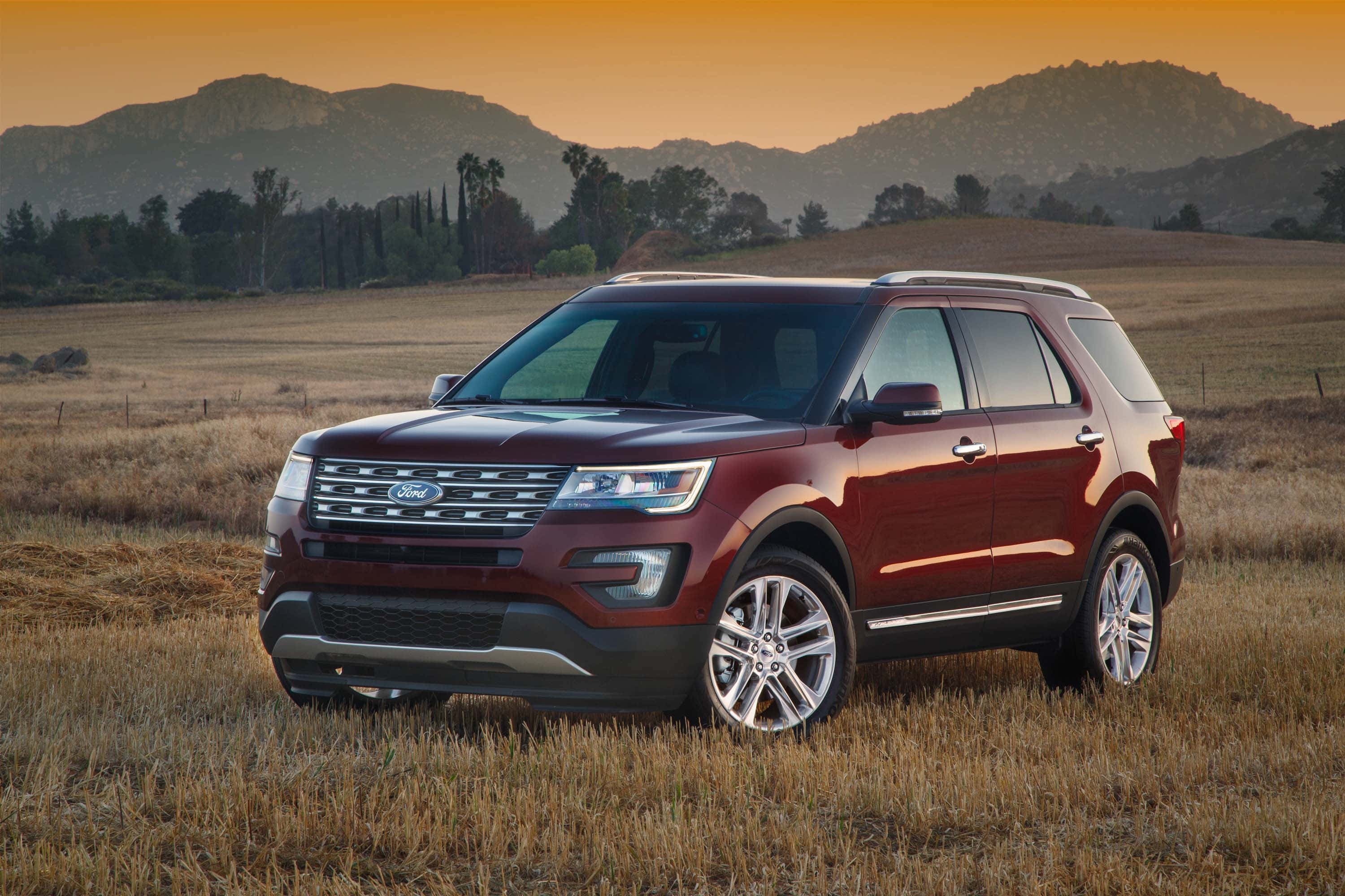 Ford Explorer 桌布 壁紙 — 一輛酒紅色的福特探險者SUV停在夕陽下的金色田野中，背景有山脈。