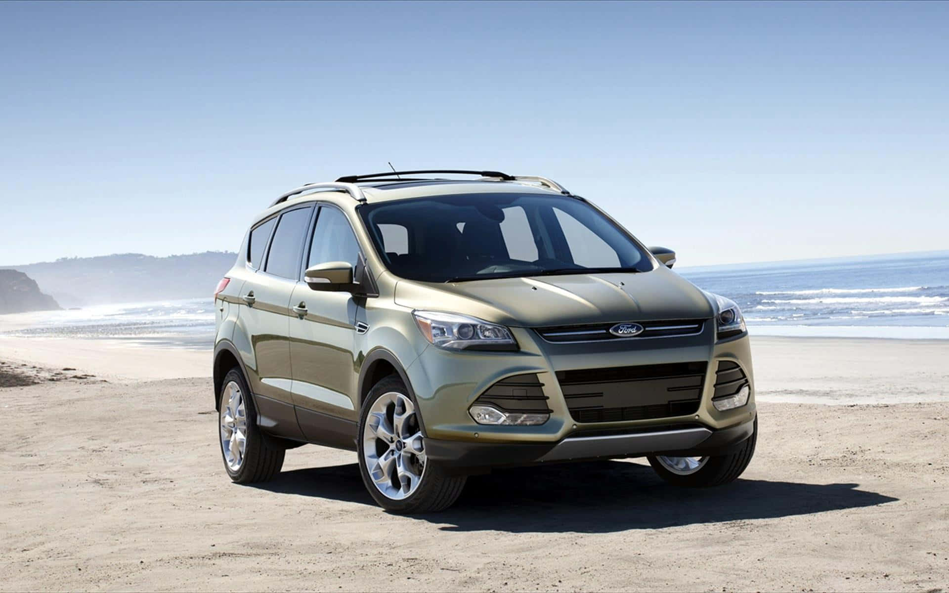 Ford Escape 桌布 壁紙 — 一輛金屬綠色的福特 Escape SUV 停泊在陽光普照的海灘上，背景有海浪和懸崖。