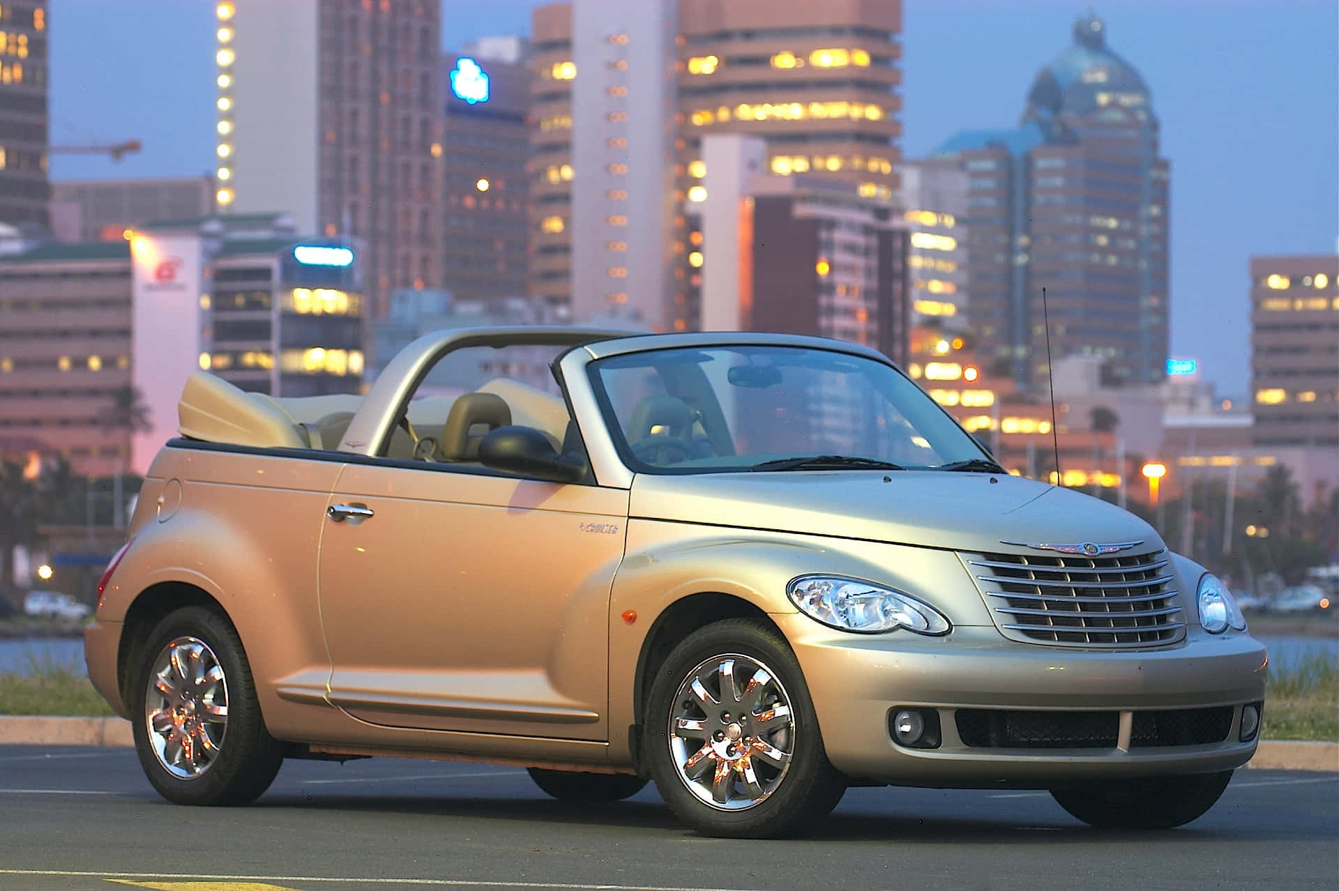 Chrysler Pt Cruiser 桌布 壁紙 — 一輛金色克萊斯勒PT Cruiser開篷車在黃昏時停泊在城市的街道上，背景是燈火通明的摩天大樓。