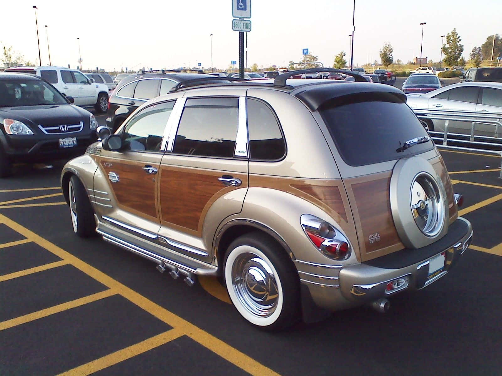 Chrysler Pt Cruiser 桌布 壁紙 — 一輛金色和木質鑲板的克萊斯勒 PT Cruiser，帶有鍍鉻裝飾，停放在陽光明媚的停車場。
