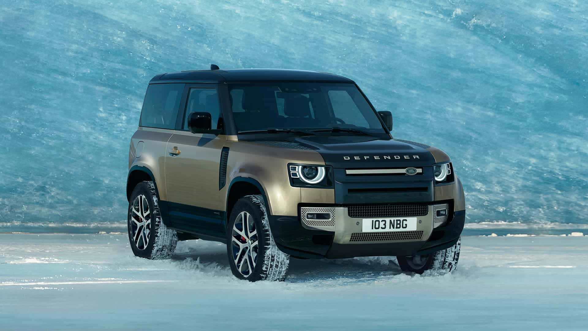 Land Rover Defender 桌布 壁紙 — 一輛金色和黑色的Land Rover Defender在雪地行駛，背景是帶有紋理的藍色冰牆。