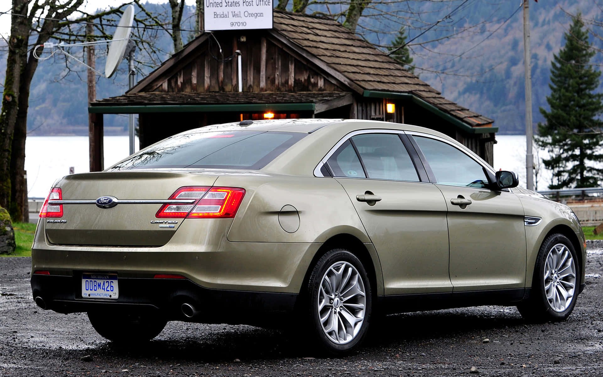 Ford Taurus 桌布 壁紙 — 一輛金色福特 Taurus 房車停泊在湖邊鄉村郵局前，背景有山巒。