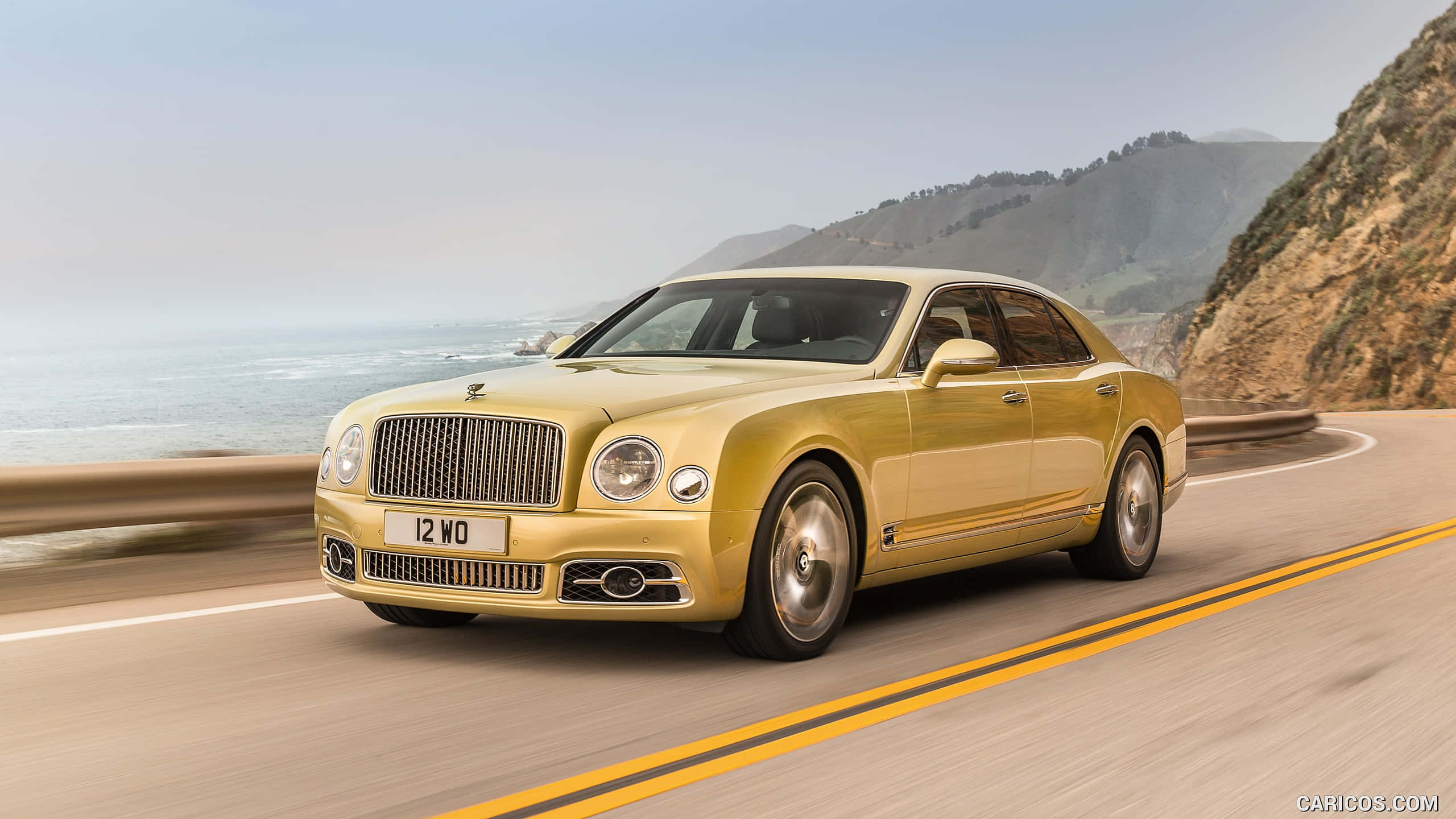 Bentley Mulsanne 桌布 壁紙 — 一輛金色賓利Mulsanne沿著海岸公路行駛，背景是海洋和懸崖。