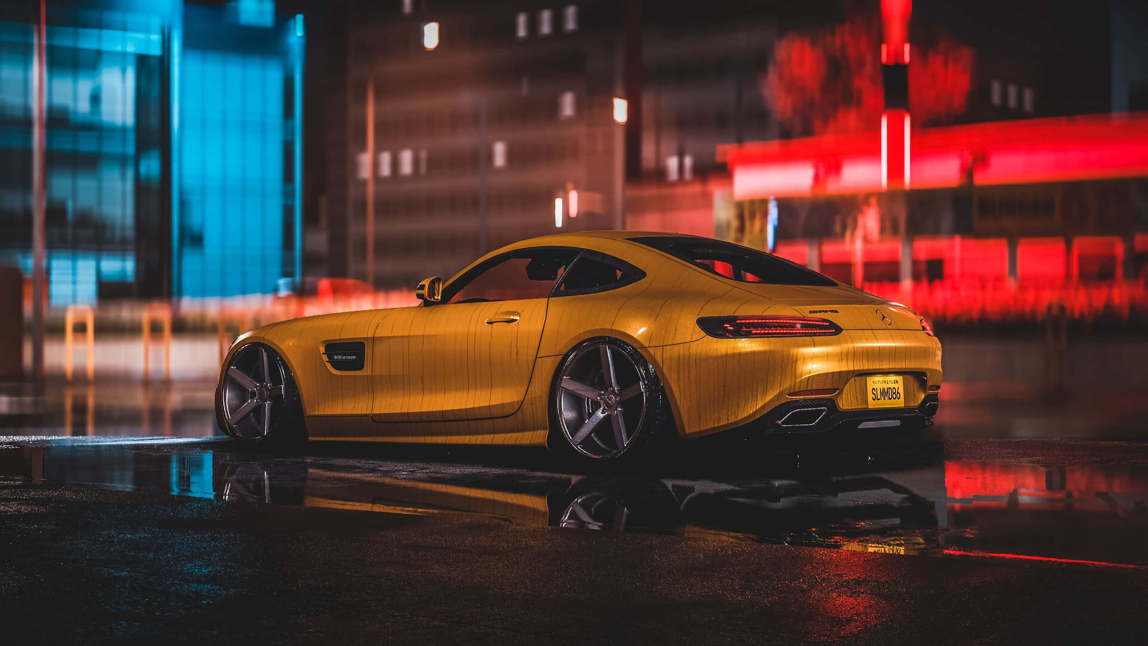 4K Mercedes 桌布 壁紙 — 一輛金色跑車在夜間濕漉漉的城市街道上閃閃發光，在黑暗天空下的水坑中反射出霓虹燈光。