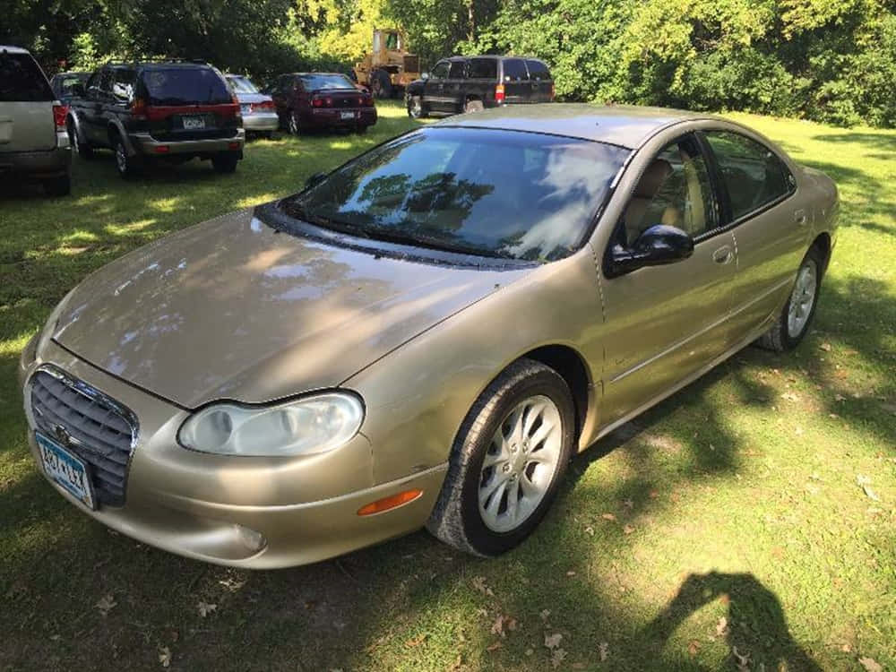 Chrysler Lhs 桌布 壁紙 — 一輛金色轎車停在草地上，陽光普照，背景有樹木和其他車輛。
