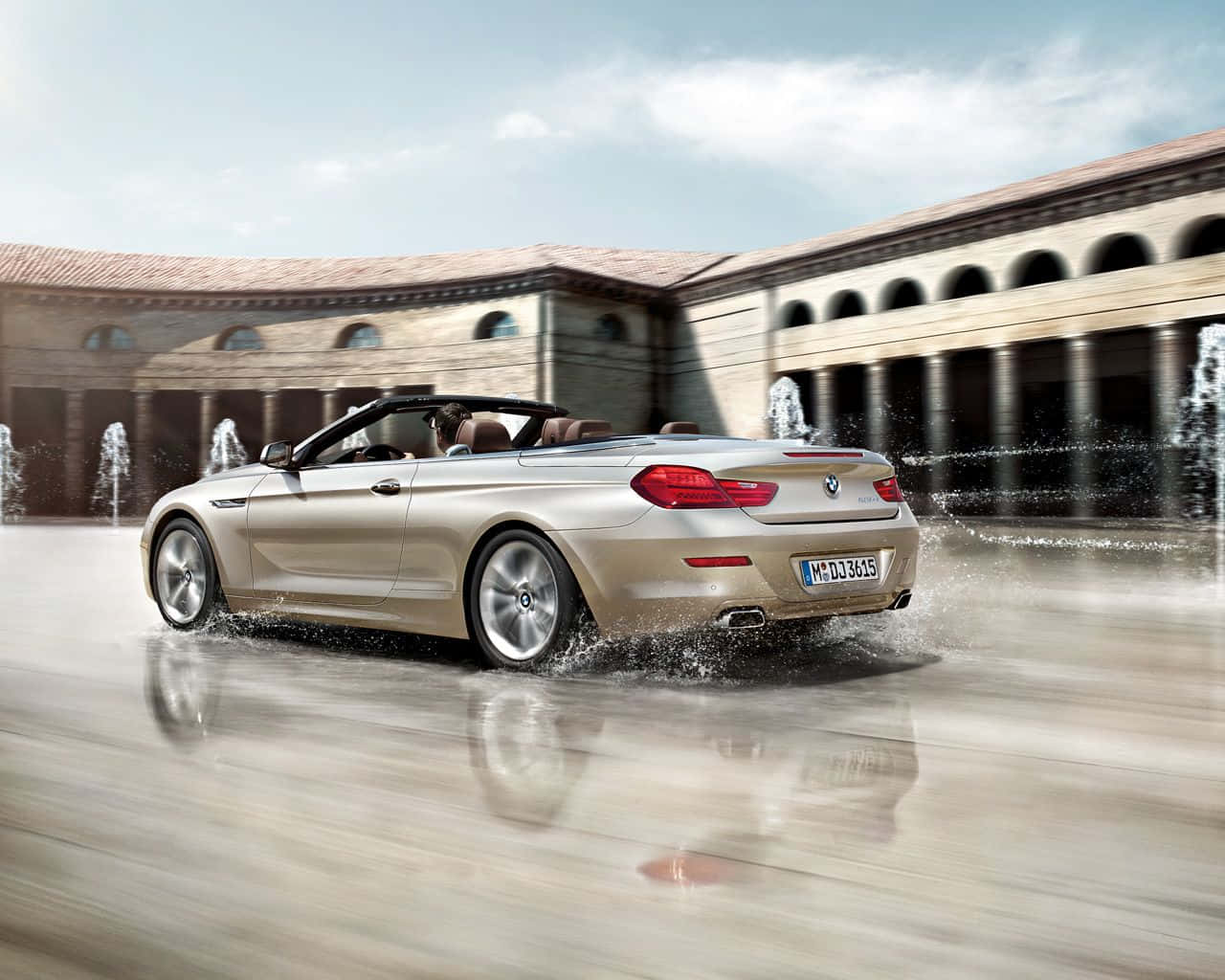 Bmw 6 Series 桌布 壁紙 — 一輛金色開篷跑車在濕漉漉的庭院中疾馳，濺起水花，噴泉在古典建築後方噴灑。