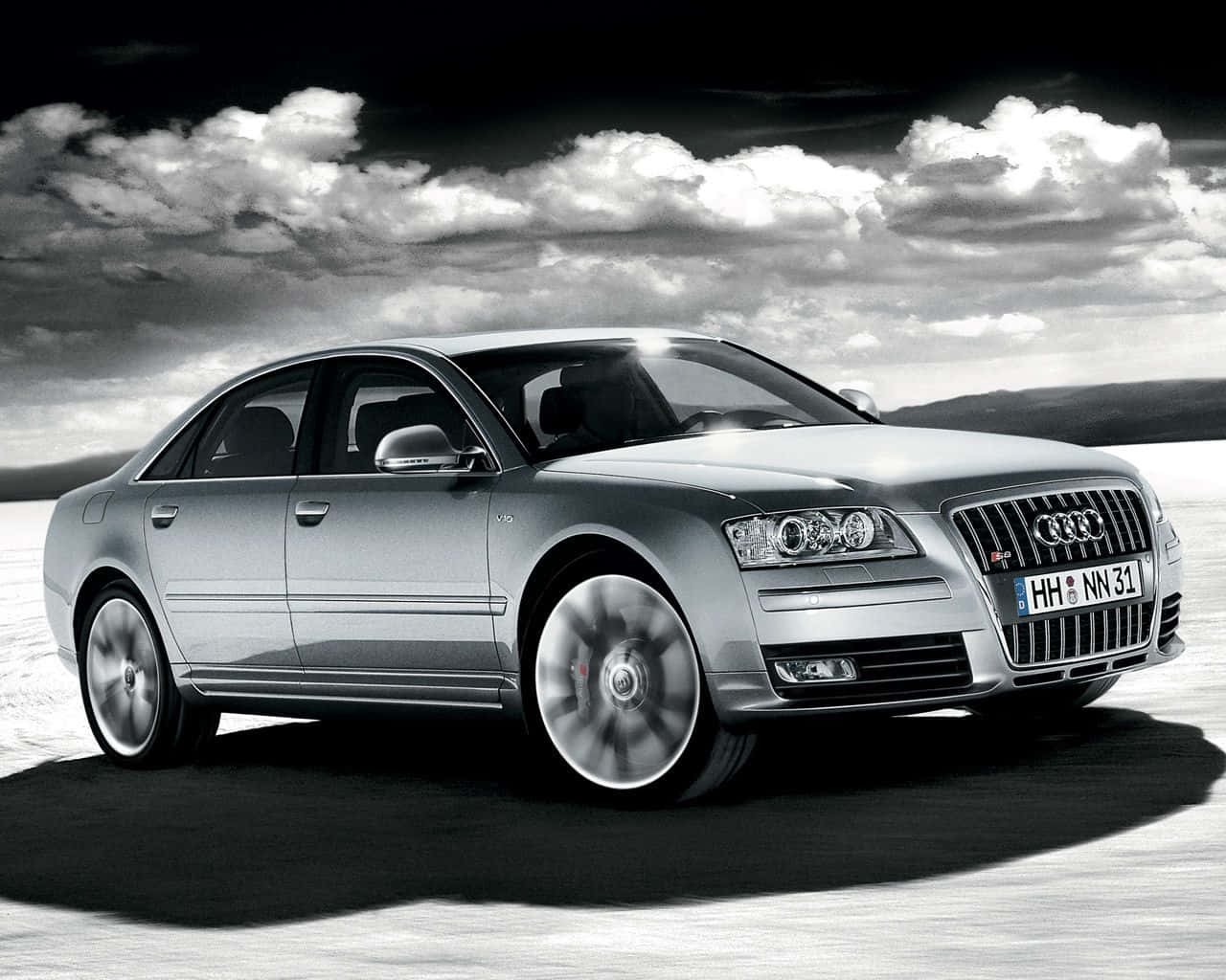 Audi S8 桌布 壁紙 — 一輛銀色 Audi 房車在戲劇性的多雲天空下，飛馳過雪原。