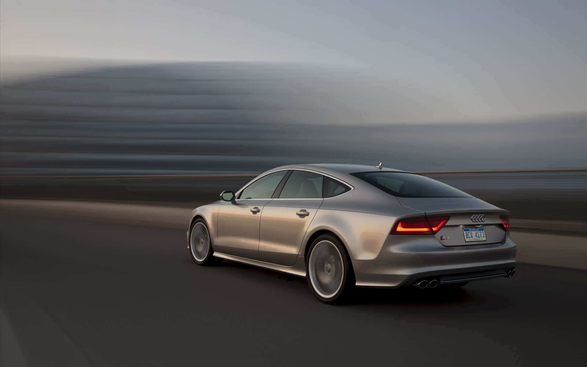 Audi S7 桌布 壁紙 — 一輛銀色 Audi 房車在黃昏時分沿著道路疾馳，背景帶有動態模糊效果。