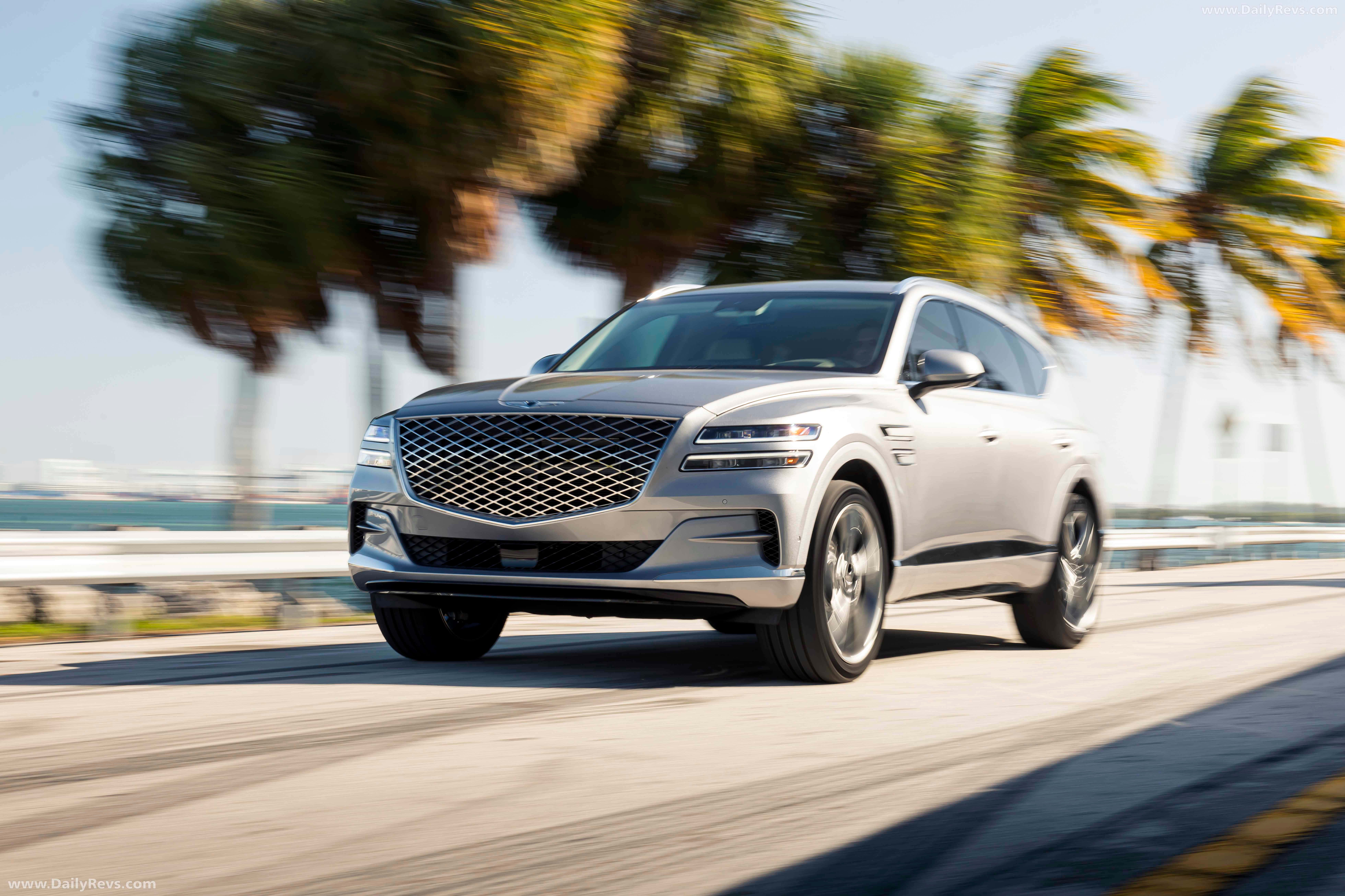 Genesis Gv80 桌布 壁紙 — 一輛銀色 Genesis GV80 SUV 沿著海岸道路疾馳，棕櫚樹在溫暖的陽光下模糊掠過。