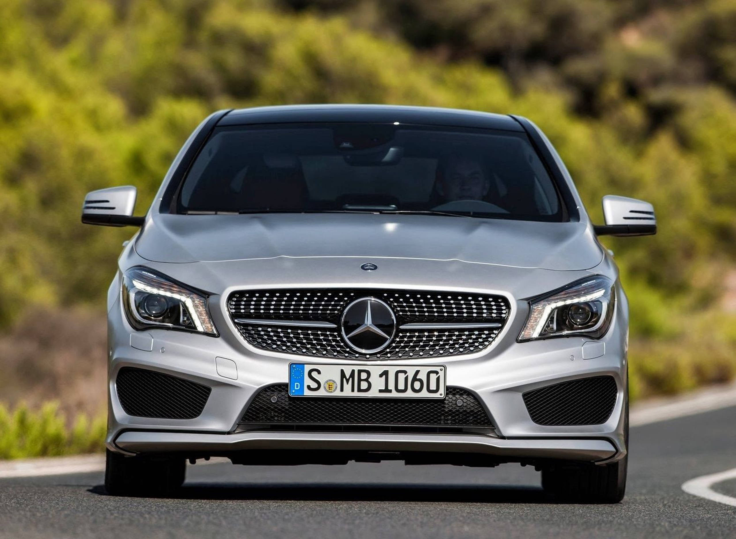 HD 桌布 壁紙 — 一輛銀色 Mercedes-Benz CLA 跑車在蜿蜒的道路上行駛，背景是模糊的綠色樹葉。