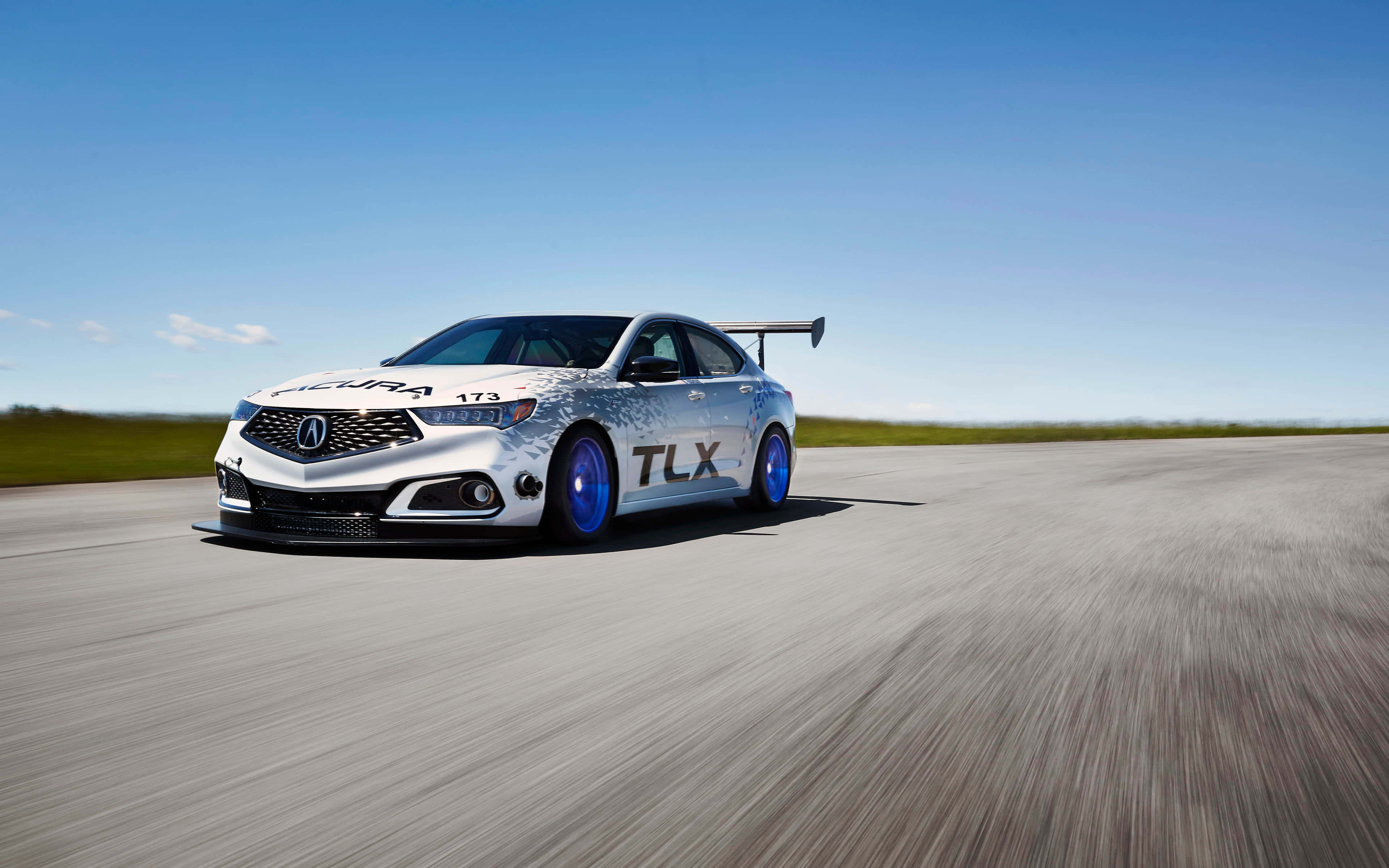 Acura Tlx 桌布 壁紙 — 一輛銀色Acura TLX賽車配備藍色輪圈，在晴朗藍天下於陽光普照的瀝青賽道上飛馳。