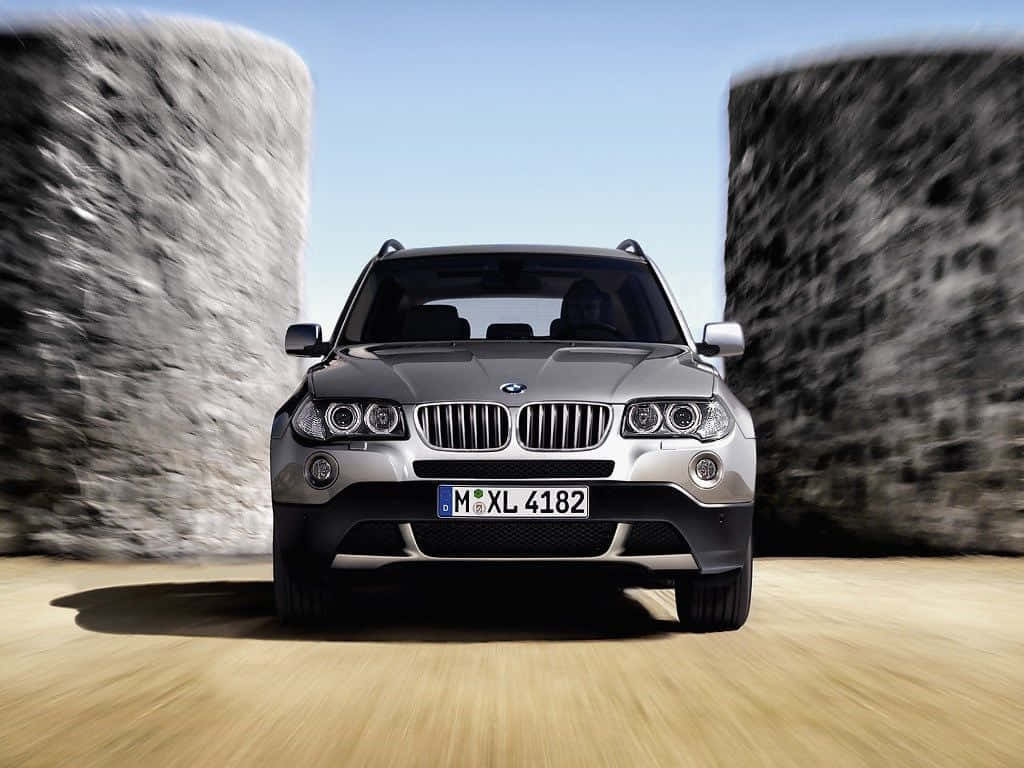 Bmw X3 桌布 壁紙 — 一輛銀色BMW X5 SUV在石牆和木地板上，於晴朗藍天下帶着動態模糊向前飛馳。