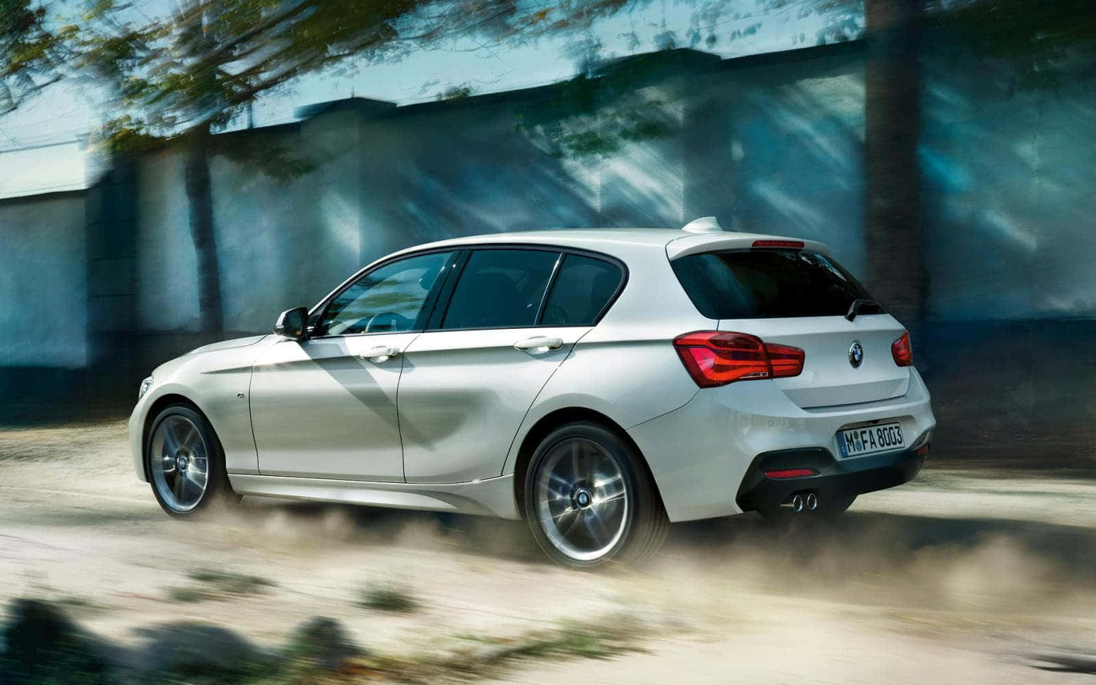 Bmw 1 Series 桌布 壁紙 — 一輛銀色BMW掀背車在塵土飛揚的道路上行駛，帶有動態模糊效果，背景有樹木。