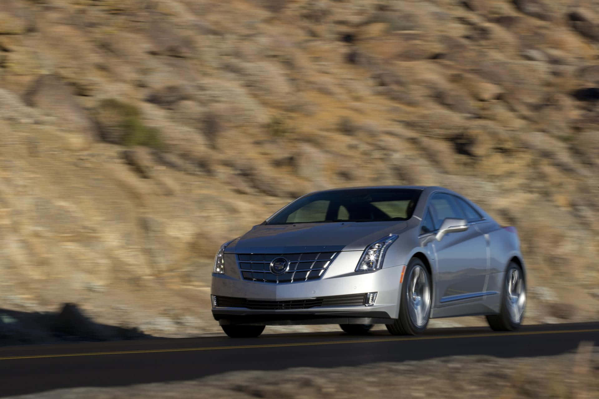 Cadillac Elr 桌布 壁紙 — 一輛銀色Cadillac ELR雙門跑車在蜿蜒的山路上疾馳，背景是模糊的岩石地形。
