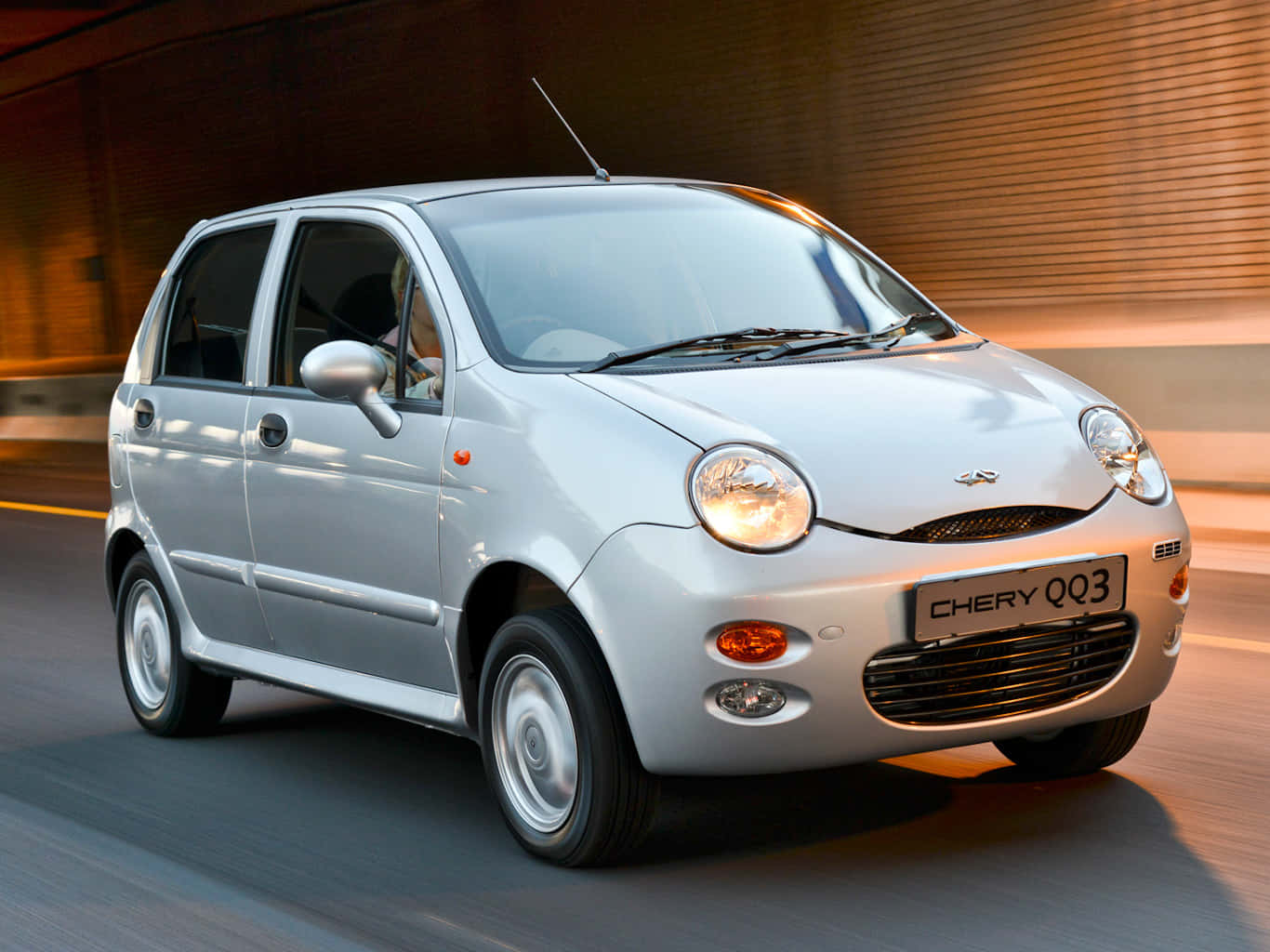 Chery 桌布 壁紙 — 一輛銀色Chery QQ3小型車在黃金時段溫暖的環境光線下，在模糊的城市道路上疾馳。