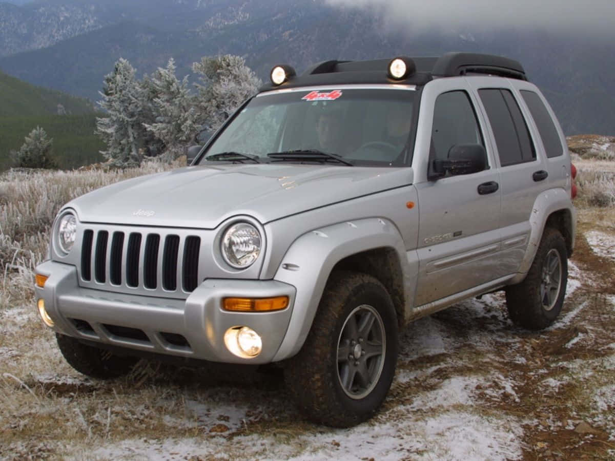 Jeep Liberty 桌布 壁紙 — 一輛銀色Jeep Cherokee在雪覆蓋的山地田野中準備就緒，背景是霜凍的樹木和霧氣籠罩的山峰。