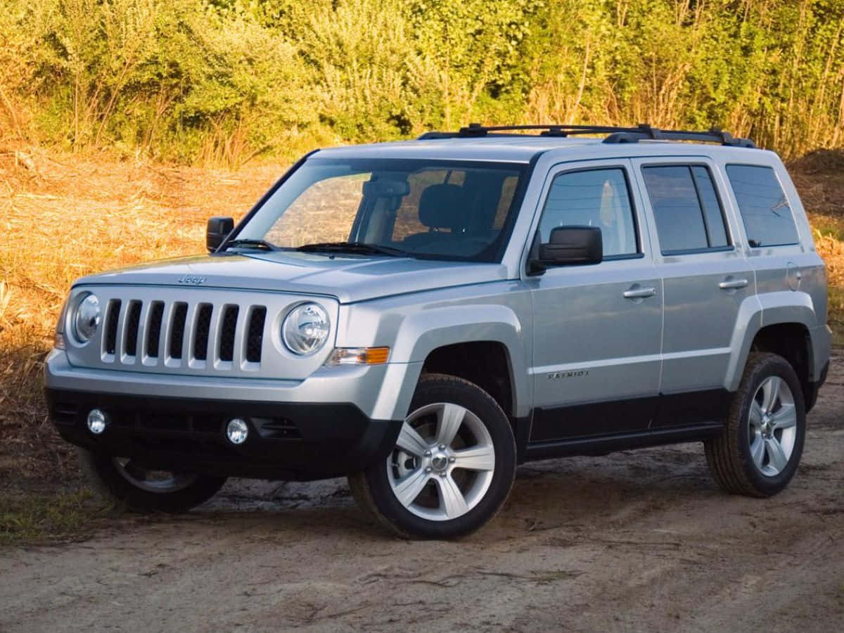 Jeep Patriot 桌布 壁紙 — 一輛銀色Jeep Patriot SUV停泊在泥濘小徑上，背景有金色樹葉和綠色灌木。