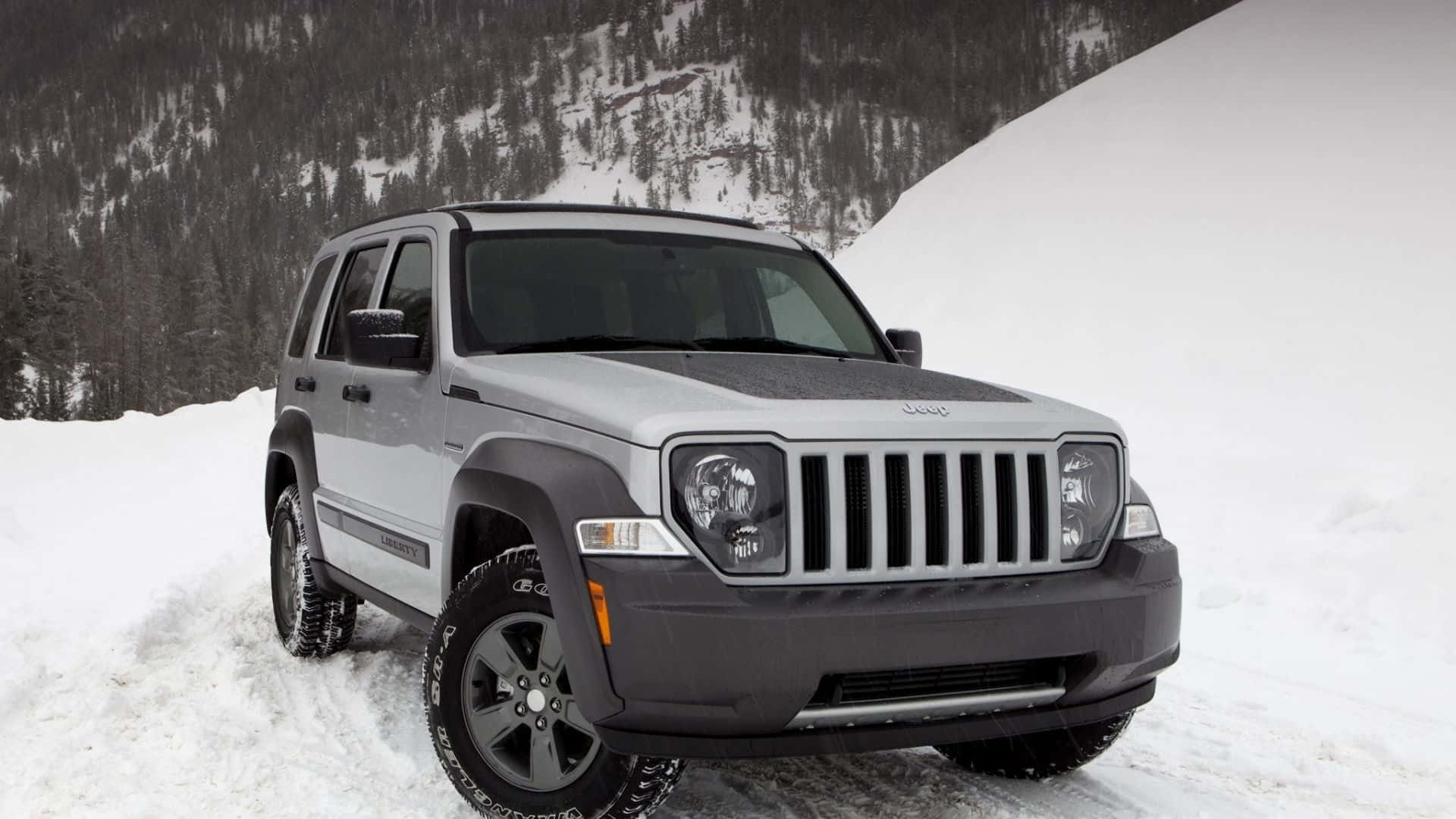 Jeep Liberty 桌布 壁紙 — 一輛銀色Jeep Wrangler在雪地山路行駛，背景有常青樹和積雪覆蓋的山坡。