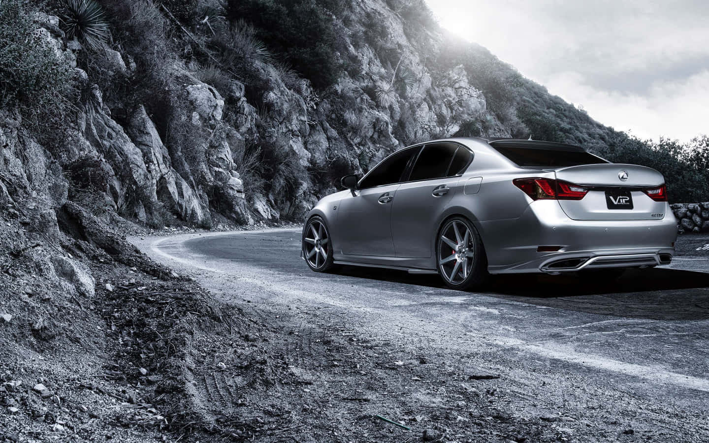 Lexus Gs 桌布 壁紙 — 一輛銀色Lexus房車在陰天下行駛於蜿蜒的山路，兩旁是崎嶇的懸崖和稀疏的植被。