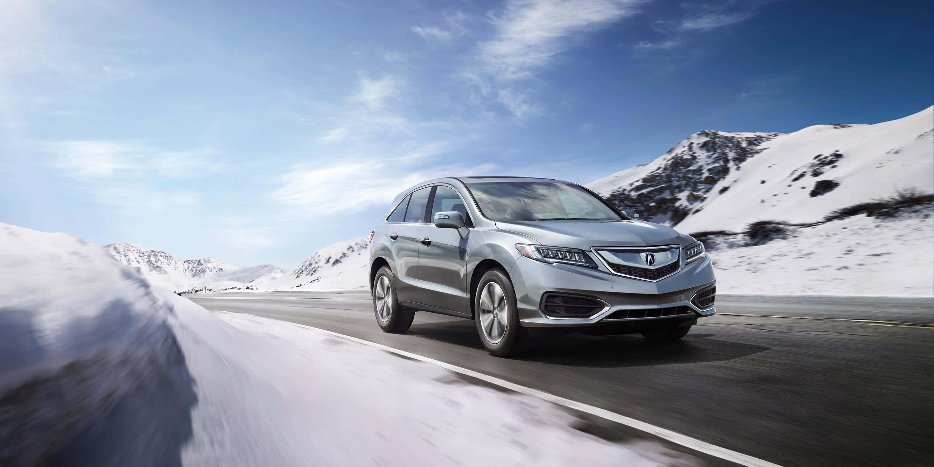 Acura Mdx 桌布 壁紙 — 一輛銀色SUV在晴朗藍天下，沿著蜿蜒的山路行駛，兩旁是白雪覆蓋的山峰。