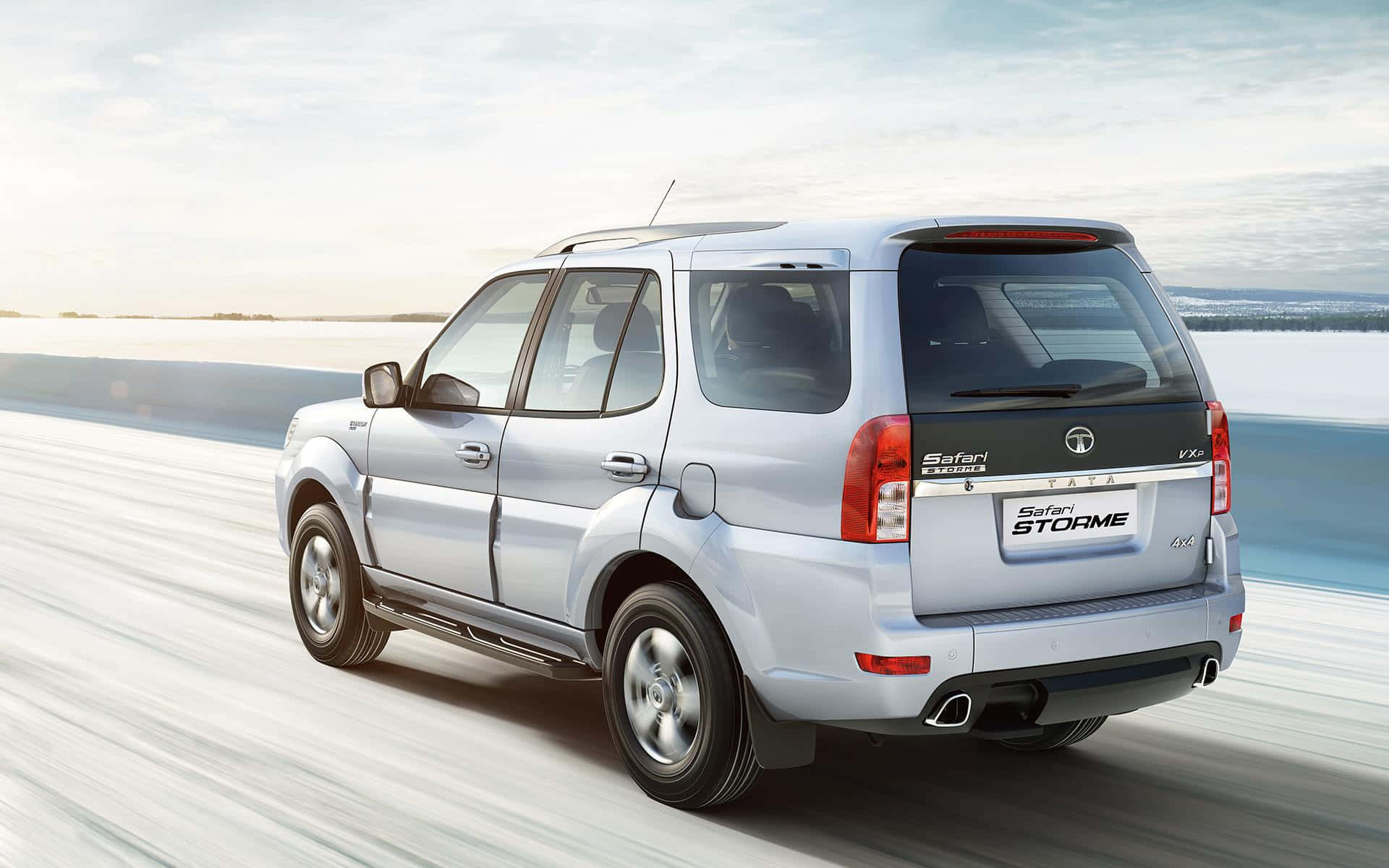 Tata Motors 桌布 壁紙 — 一輛銀色Tata Safari Storme SUV在明亮天空下，沿著積雪道路疾馳，帶有模糊動態效果。