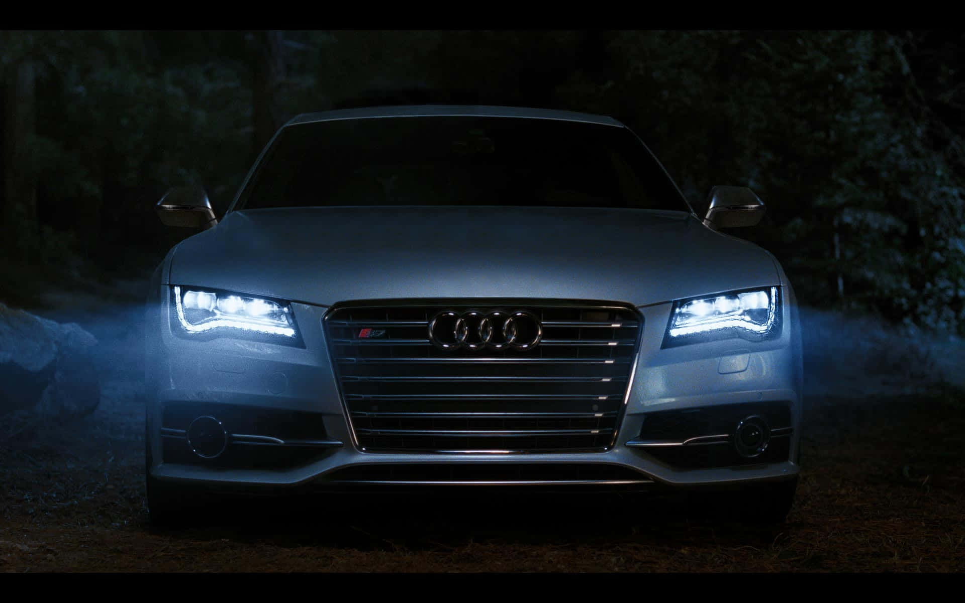 Audi S7 桌布 壁紙 — 一輛銀色奧迪S7跑車，車頭燈閃爍，照亮了夜晚黑暗的森林小徑。