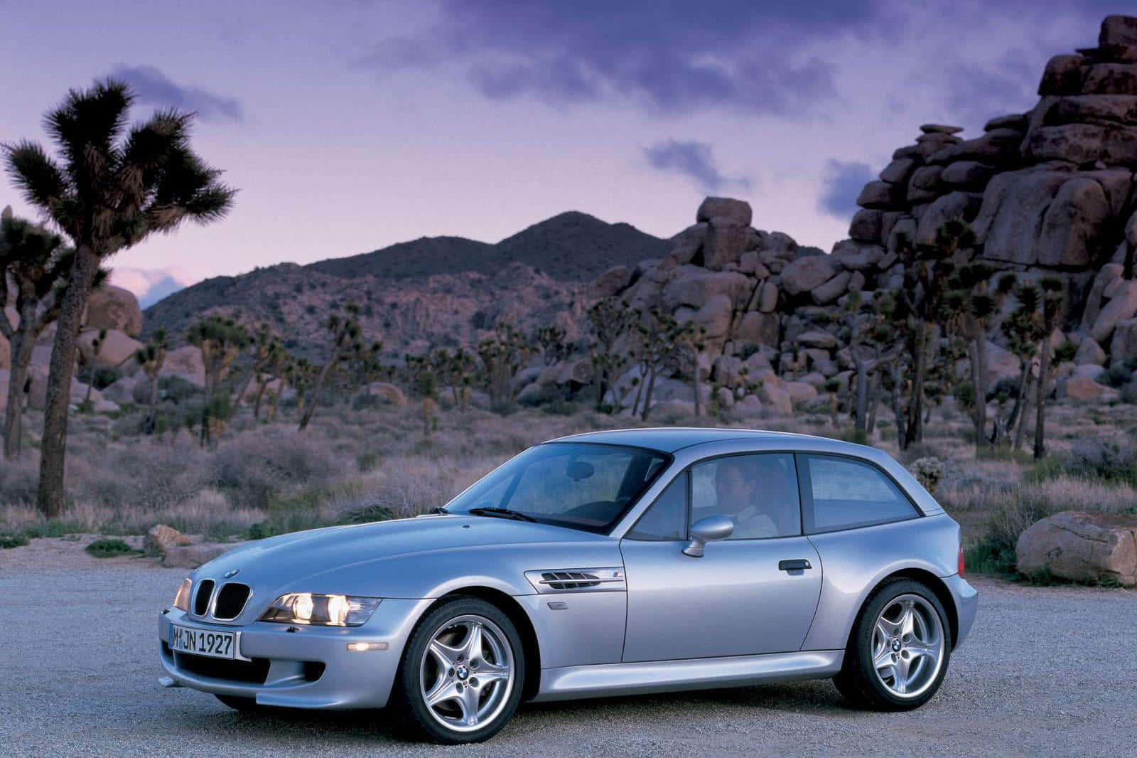 Bmw Z3 桌布 壁紙 — 一輛銀色寶馬Z3開篷跑車停泊在暮色中的沙漠碎石路上，背景有約書亞樹和岩石山丘。