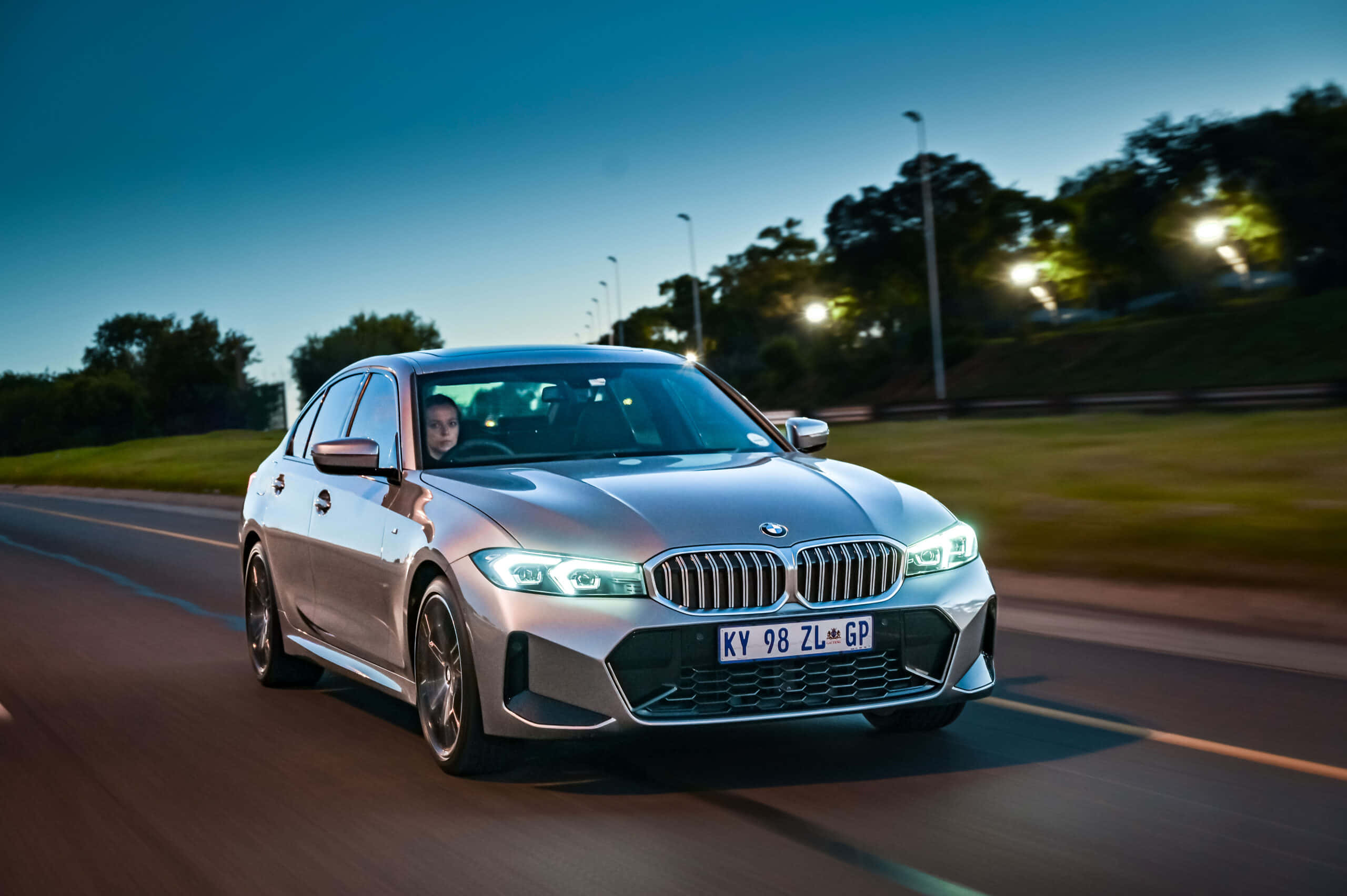Bmw 3 Series 桌布 壁紙 — 一輛銀色寶馬房車在暮色道路上疾馳，車頭燈閃爍，周圍模糊。