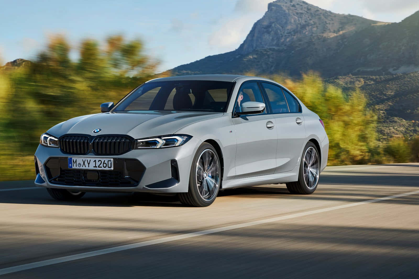 Bmw 3 Series 桌布 壁紙 — 一輛銀色寶馬房車在清晰藍天下沿著山路疾馳，周圍有模糊的綠化和岩石山峰。