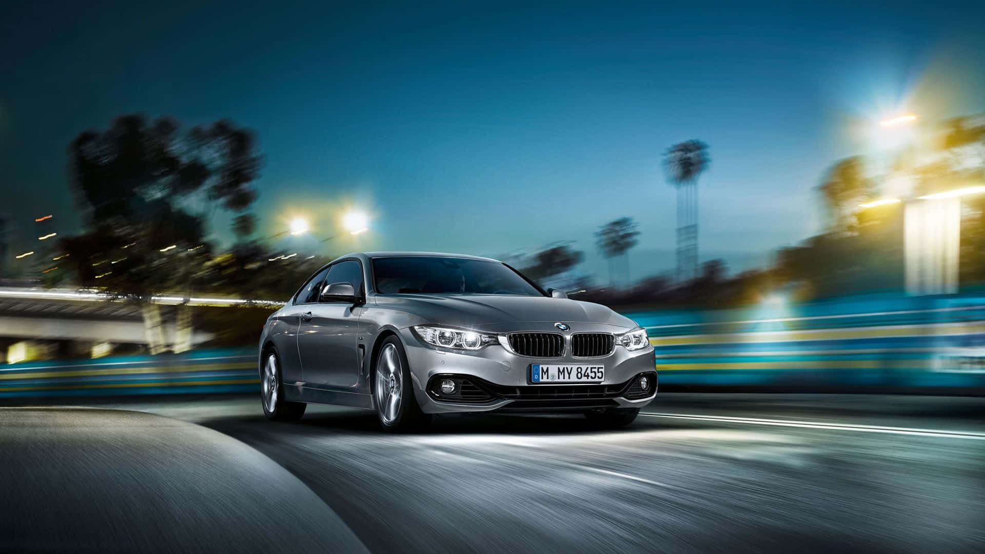 Bmw 4 Series 桌布 壁紙 — 一輛銀色寶馬轎跑車在黃昏時分沿著模糊的城市道路飛馳，背景是發光的街燈和棕櫚樹。