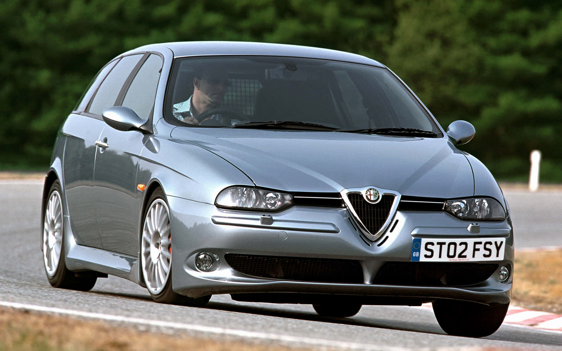 Alfa Romeo 156 桌布 壁紙 — 一輛銀色愛快羅密歐147掀背車在蜿蜒的道路上行駛，背景是茂密的綠樹。