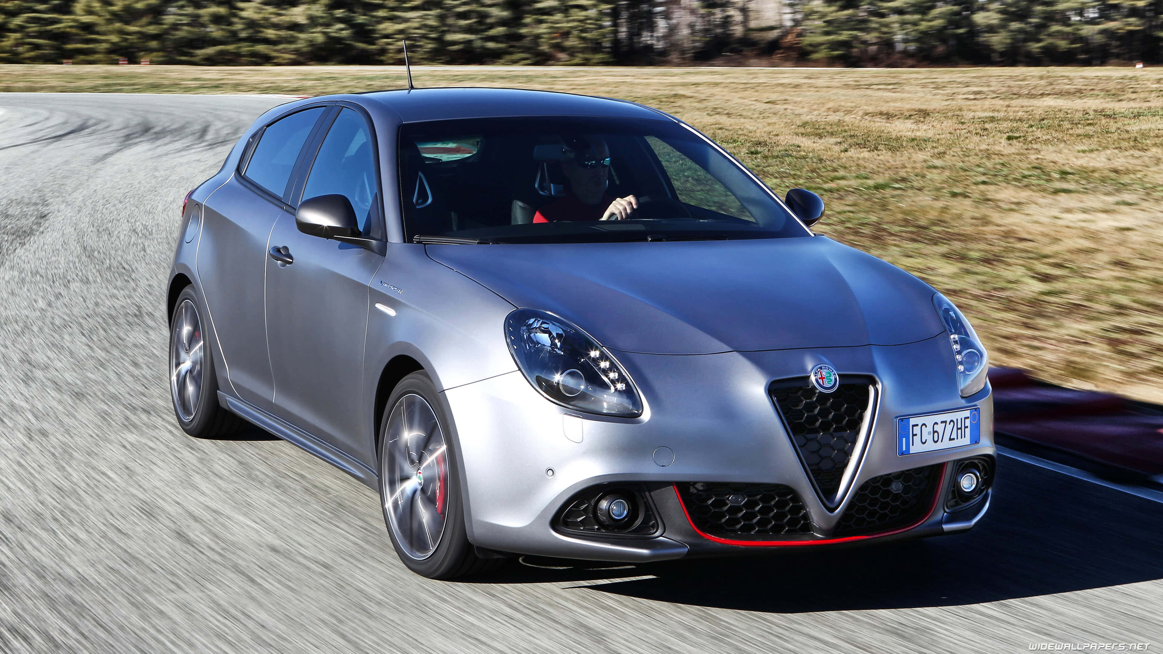 Alfa Romeo Giulietta 桌布 壁紙 — 一輛銀色愛快羅密歐Giulietta跑車在蜿蜒的道路上飛馳，背景是模糊的草地。