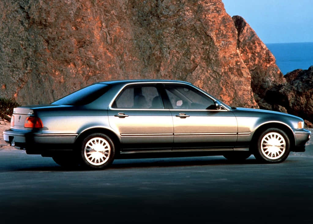 Acura Legend 桌布 壁紙 — 一輛銀色房車停泊在日落時分俯瞰海洋的巨型岩石懸崖旁邊的海岸公路上。