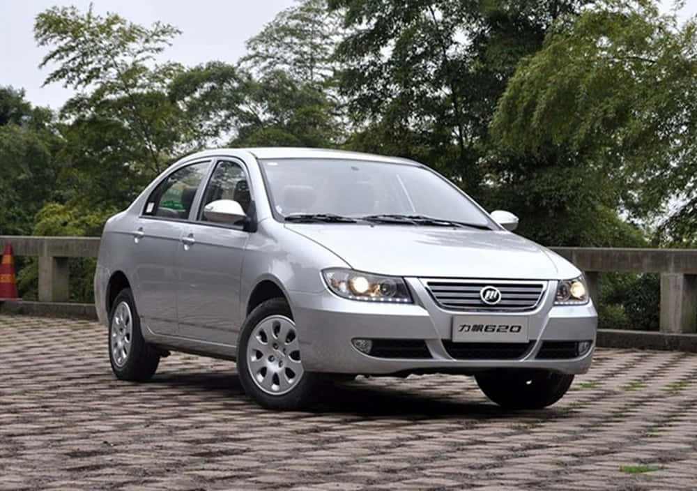 Lifan 桌布 壁紙 — 一輛銀色房車停泊在鋪砌路面上，背景是茂密的綠樹，天空多雲。