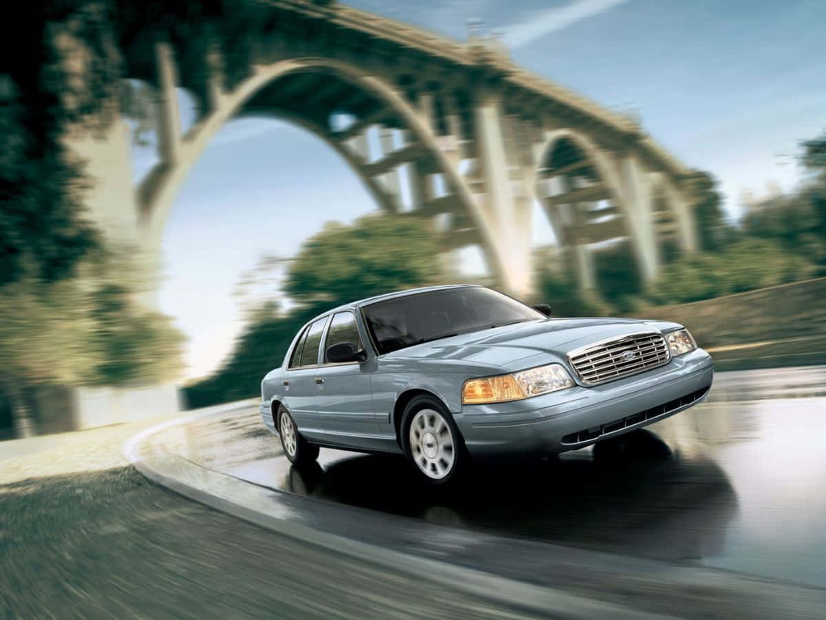 Ford Crown Victoria 桌布 壁紙 — 一輛銀色房車在濕滑道路上，於石拱橋下疾馳，周圍呈現動態模糊效果。