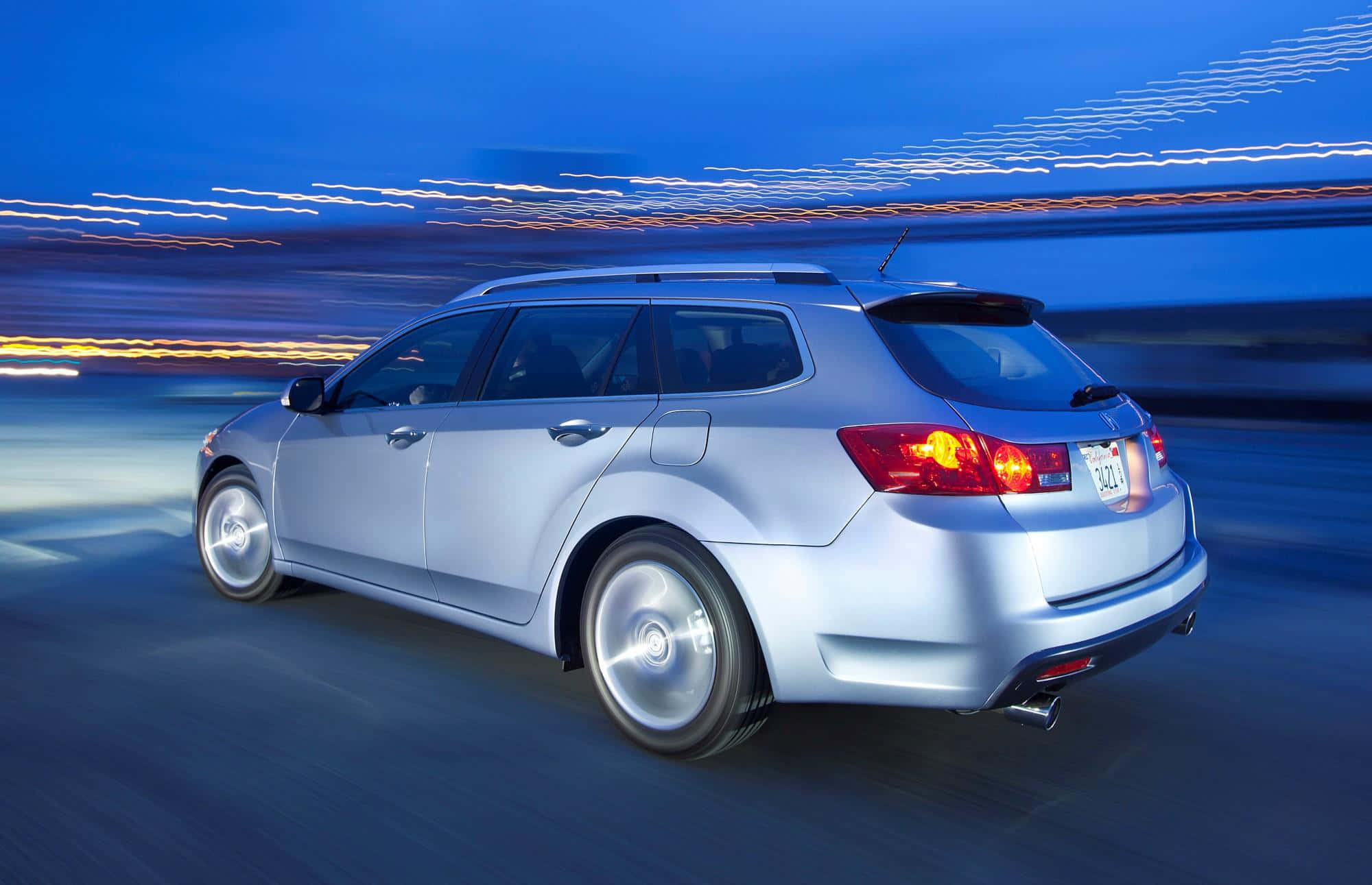 Acura Tsx 桌布 壁紙 — 一輛銀色旅行車在暮色中疾馳，城市燈光化為條紋模糊掠過。