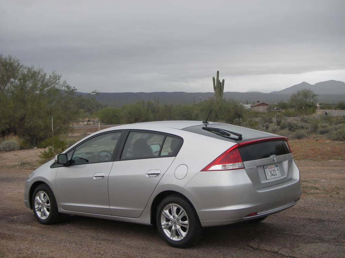 Honda Insight 桌布 壁紙 — 一輛銀色本田Insight混合動力車停在碎石上，背景是沙漠景觀，有仙人掌和遠山，天空多雲。
