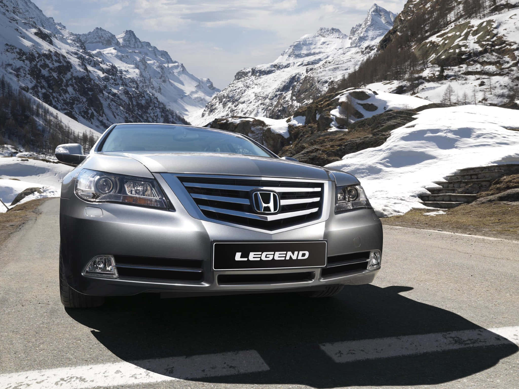 Honda Legend 桌布 壁紙 — 一輛銀色本田Legend轎車在晴朗的天空下行駛在蜿蜒的山路上，周圍是白雪皚皚的山峰。