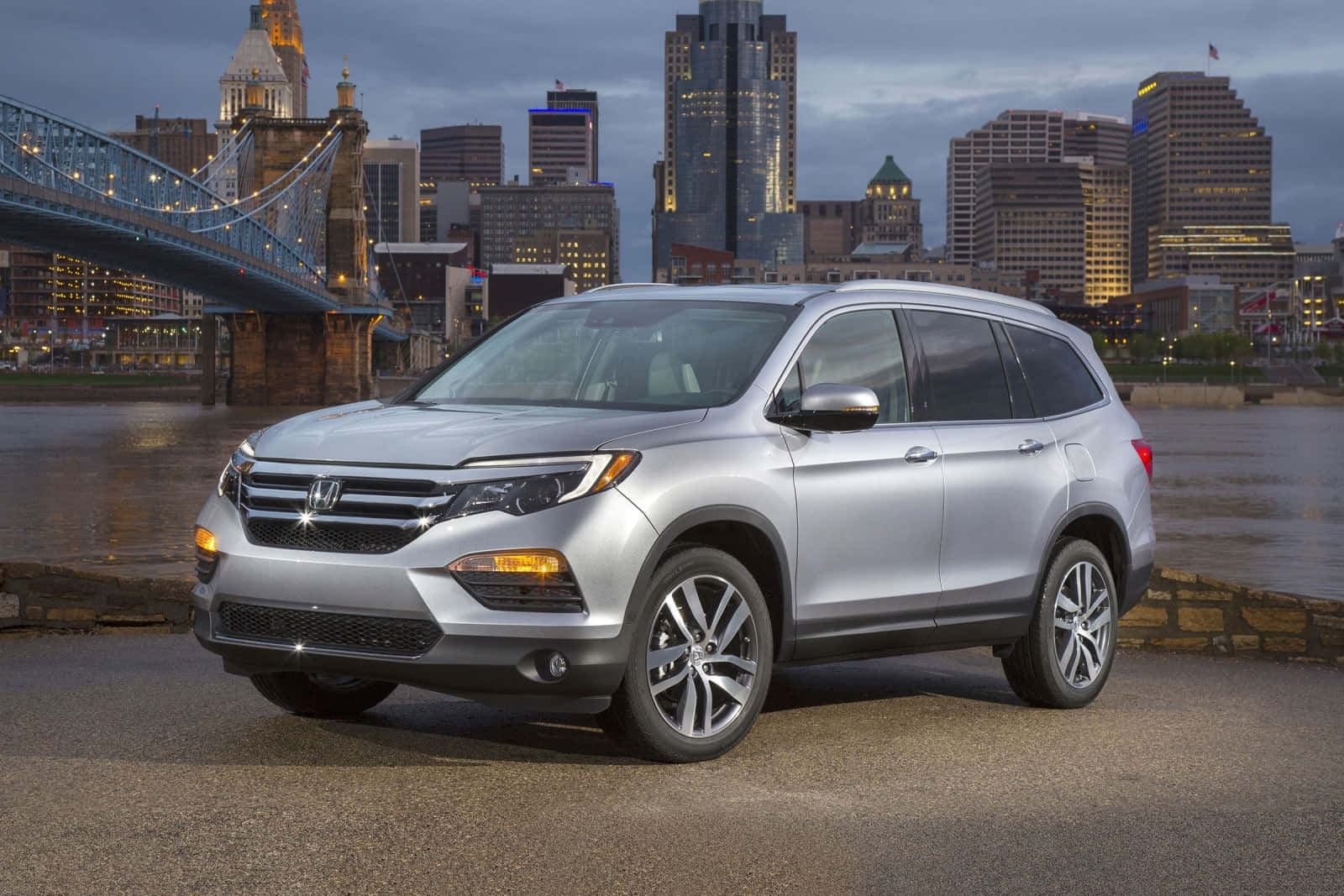 Honda Pilot 桌布 壁紙 — 一輛銀色本田Pilot SUV停泊在河邊，背景是黃昏時分燈火通明的城市天際線和橋樑。