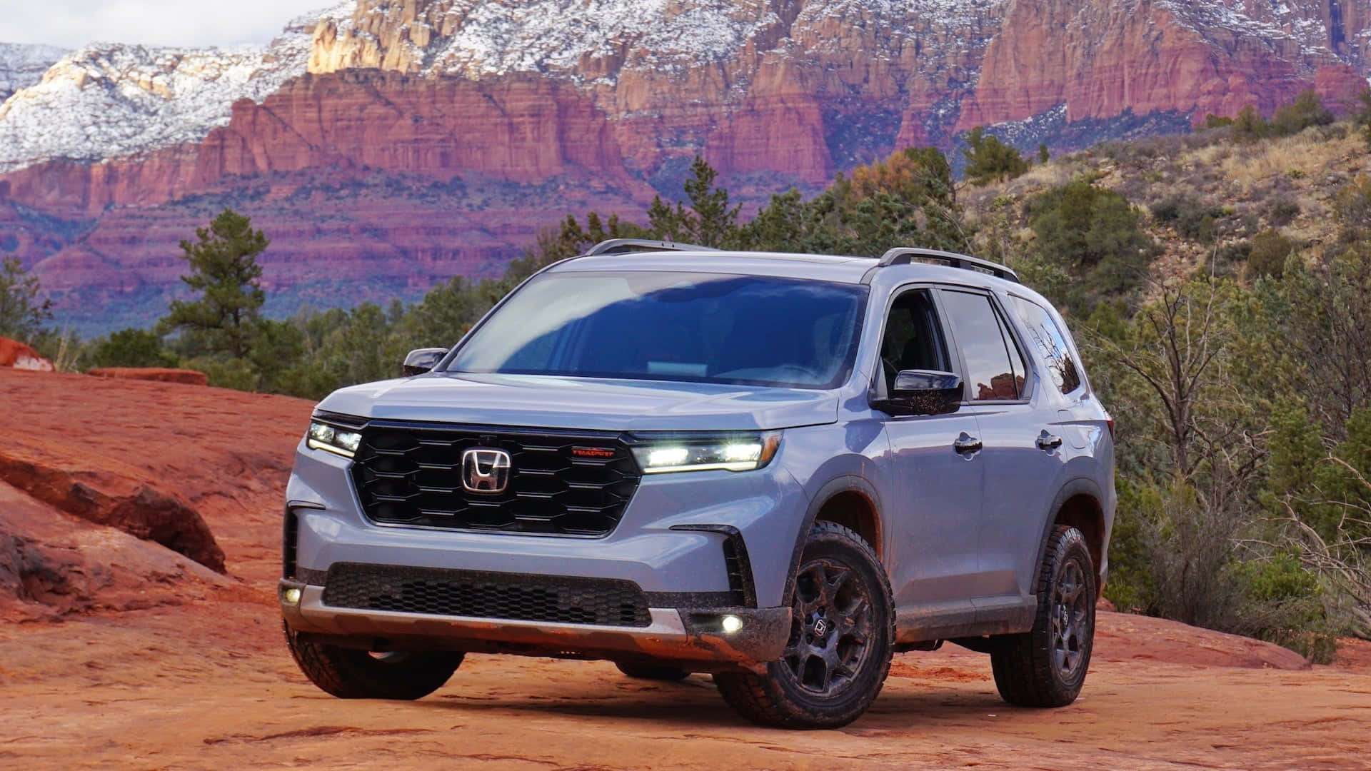 Honda Pilot 桌布 壁紙 — 一輛銀色本田Pilot SUV配黑色輪胎，停在紅色岩石地形上，背景是積雪的峽谷懸崖。