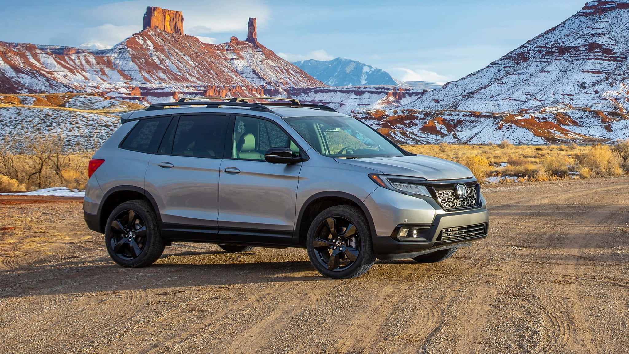 Honda Passport 桌布 壁紙 — 一輛銀色本田Pilot SUV配黑色輪圈，停泊在雪地沙漠小徑上，背景有紅色岩層。