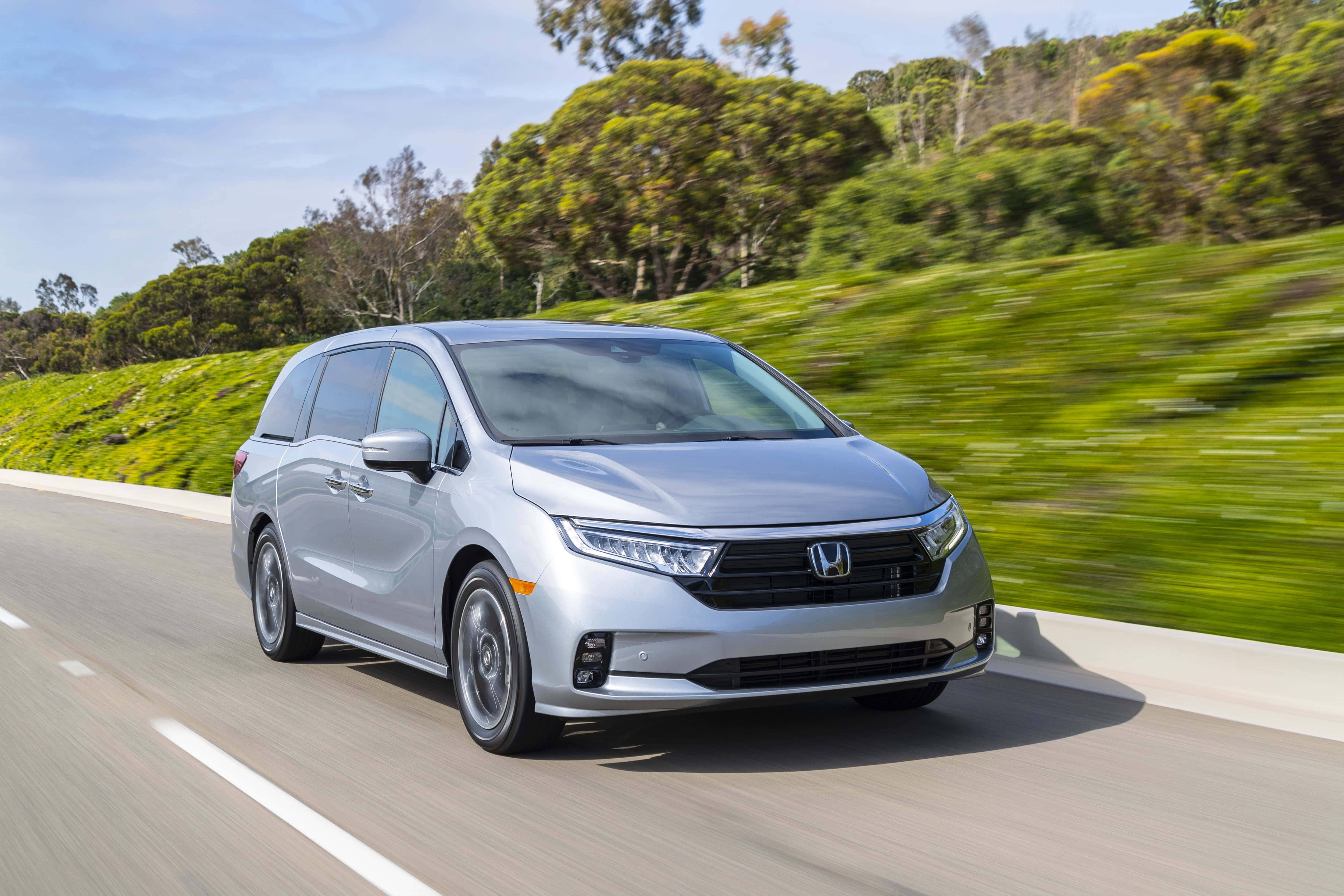 Honda Odyssey 桌布 壁紙 — 一輛銀色本田小型貨車在晴朗藍天下沿著蜿蜒道路穿過翠綠山丘飛馳。