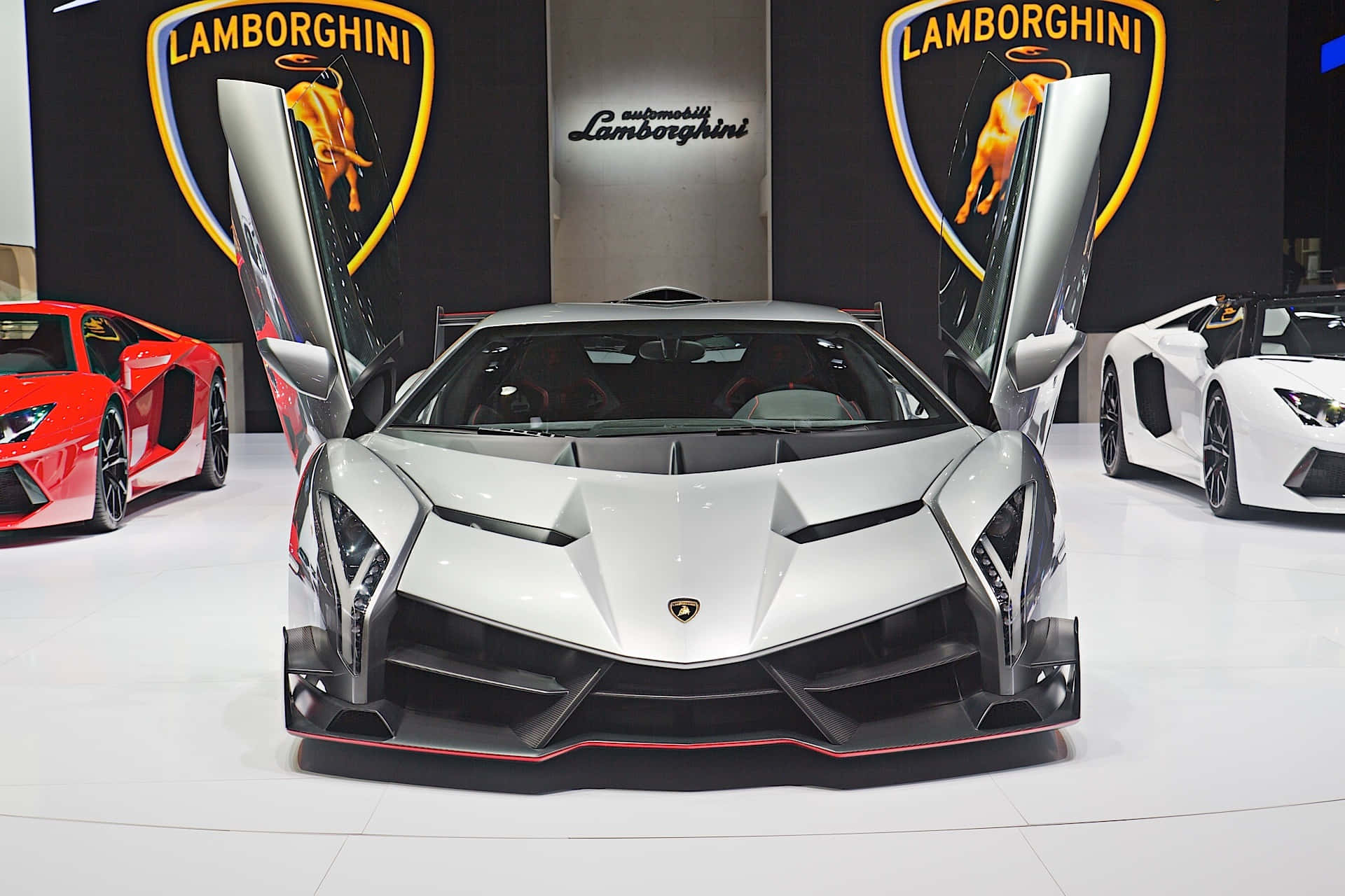 Lamborghini Veneno 桌布 壁紙 — 一輛銀色林寶堅尼打開鷗翼門，在車展上展示進取的棱角線條和紅色點綴。