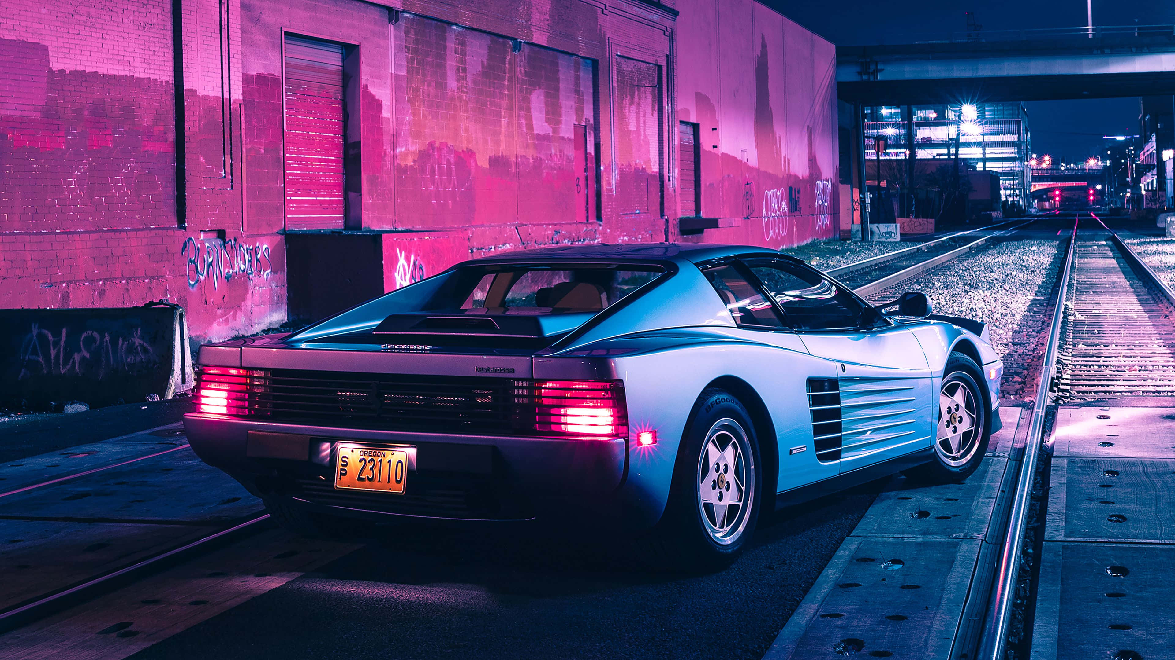 4K 法拉利 桌布 壁紙 — 一輛銀色法拉利 Testarossa 在夜間停泊在濕漉漉的火車軌道上，周圍是鮮豔的粉紅色霓虹燈。