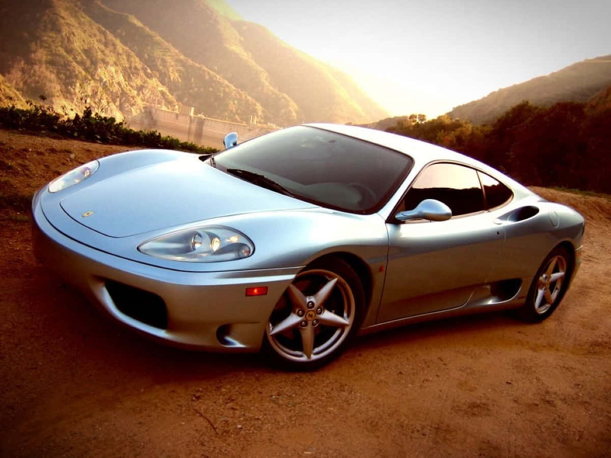 Ferrari 360 Modena 桌布 壁紙 — 一輛銀色法拉利360跑車在泥路上閃閃發光，背景是陽光普照的山脈。
