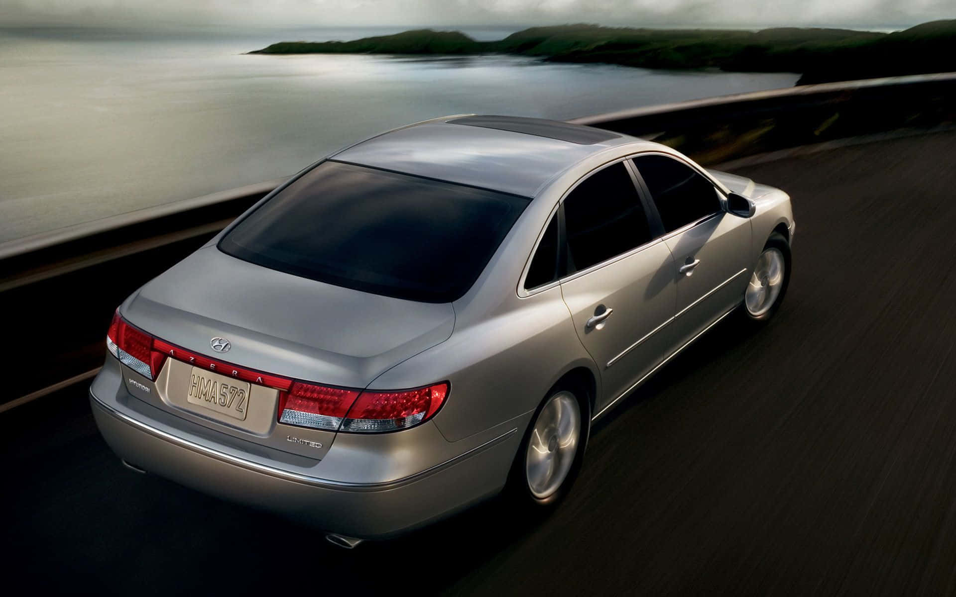 Hyundai Azera 桌布 壁紙 — 一輛銀色現代Azera轎車沿著海岸公路行駛，在霧濛濛的海洋背景下呈現模糊動態效果。